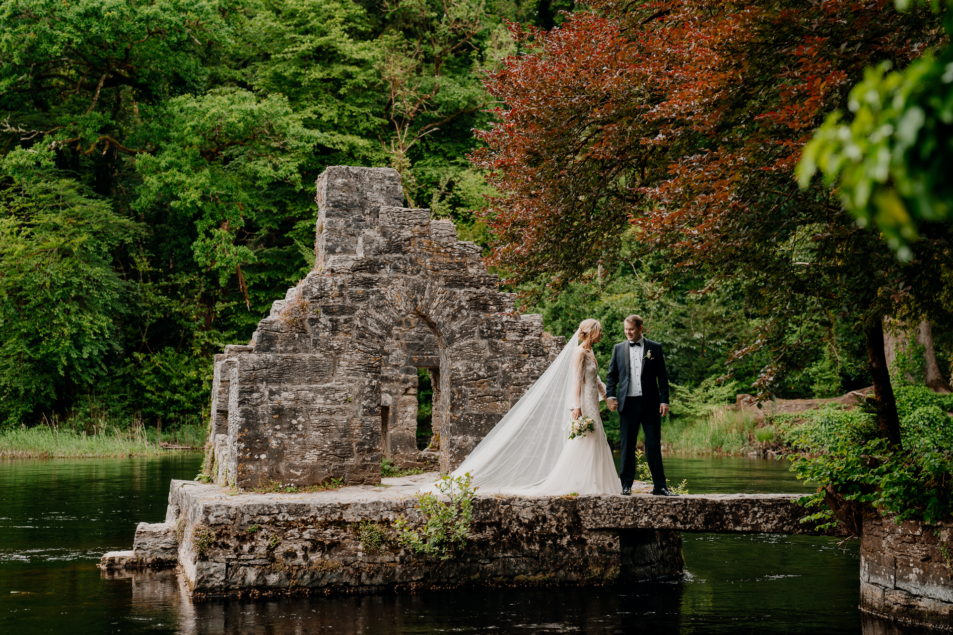 A bride and groom standing on a stone structure in a forest