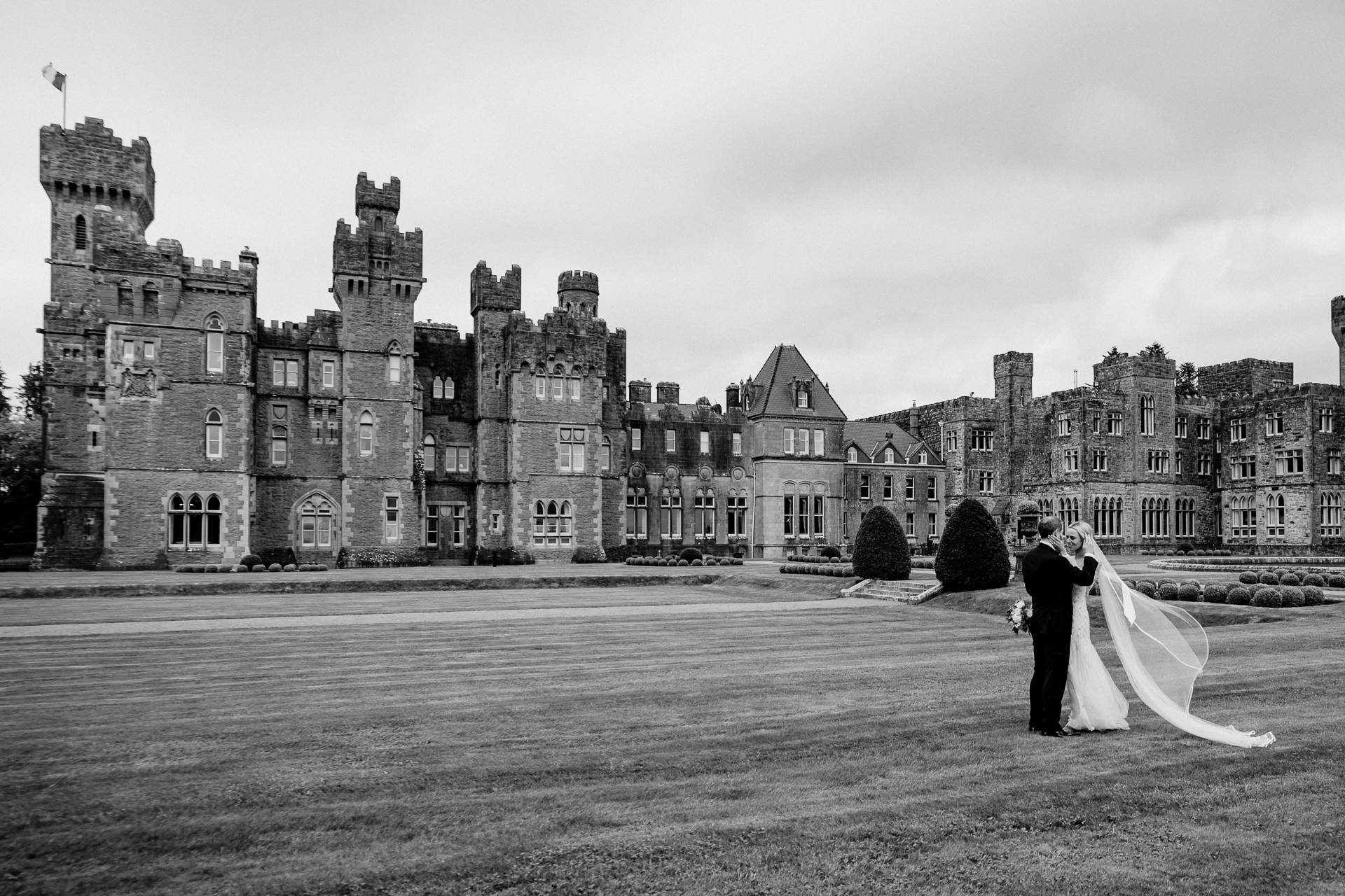 A bride and groom kissing in front of a castle