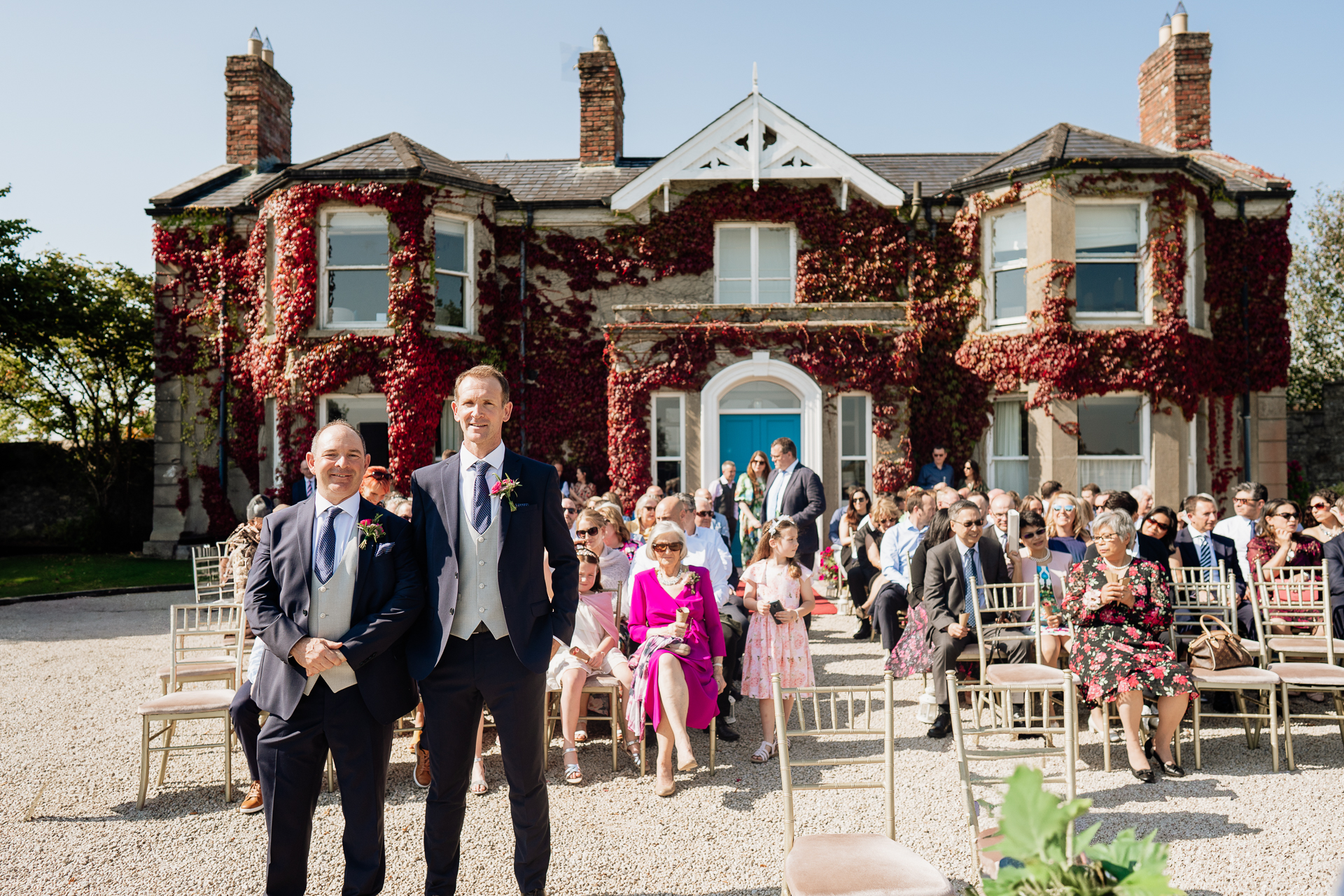 A group of men in suits walking down a stone path in front of a house