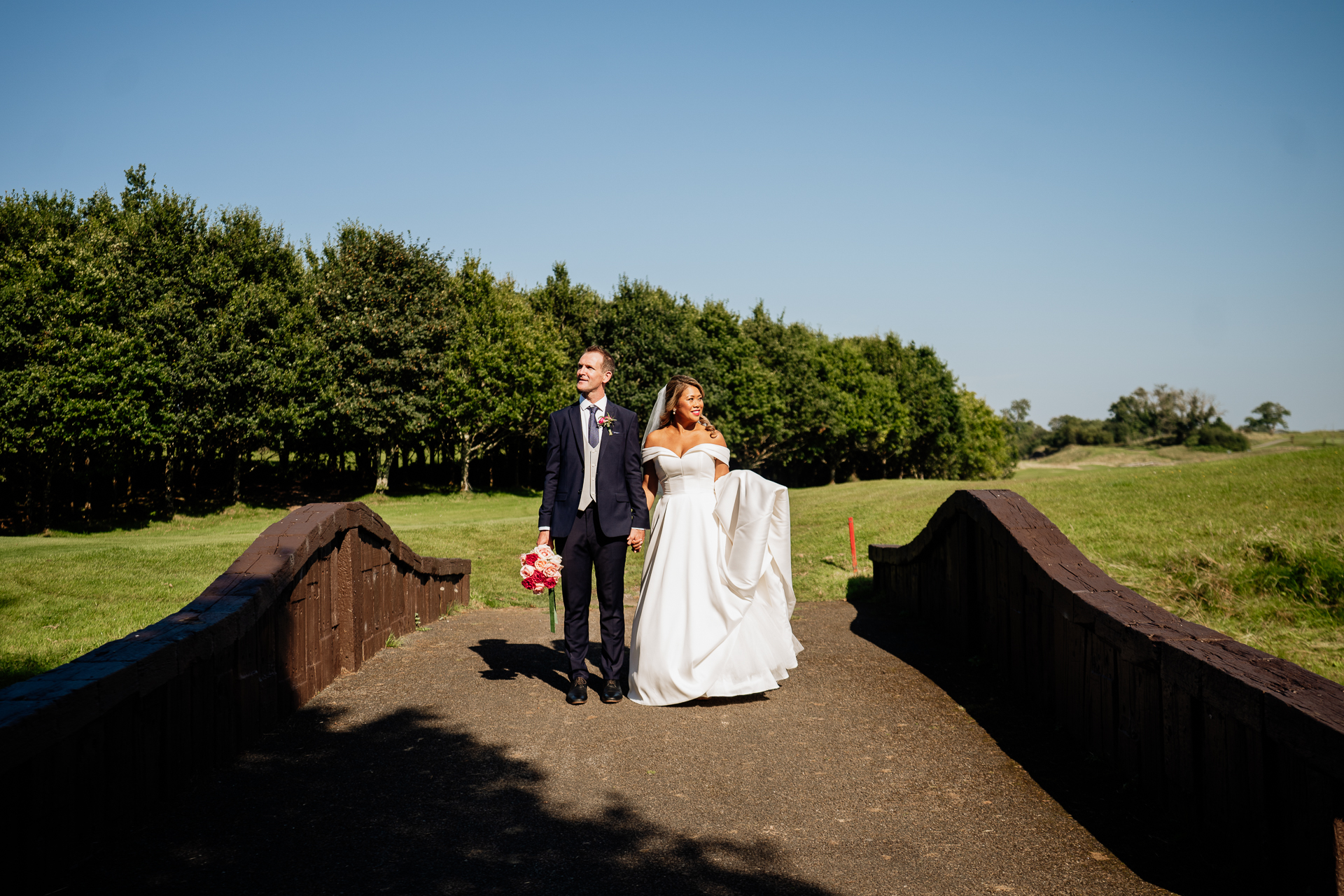 A man and woman in wedding attire standing on a bridge over a river