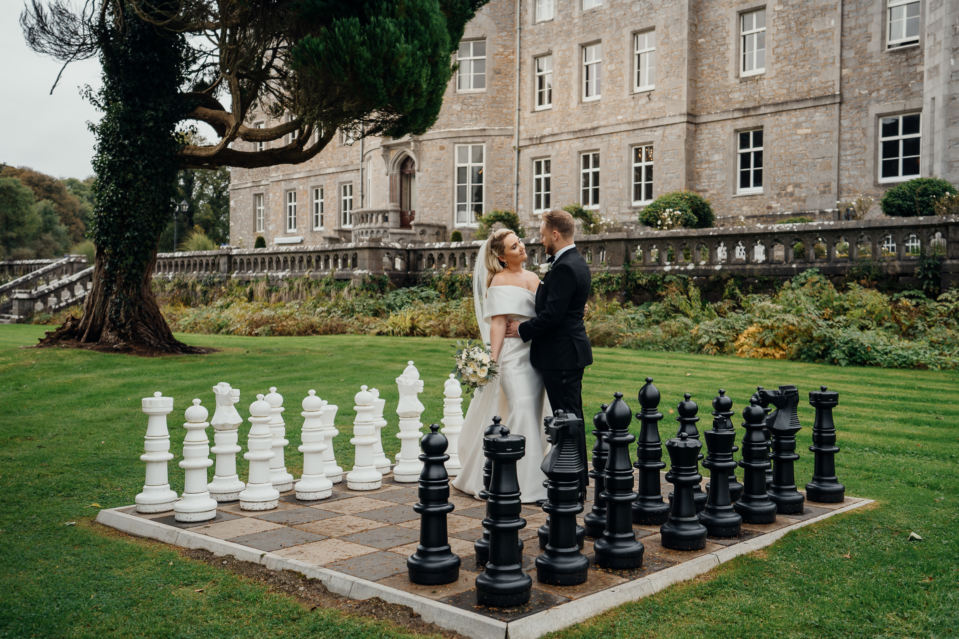 A man and woman in wedding attire standing on a gravestone in front of a building