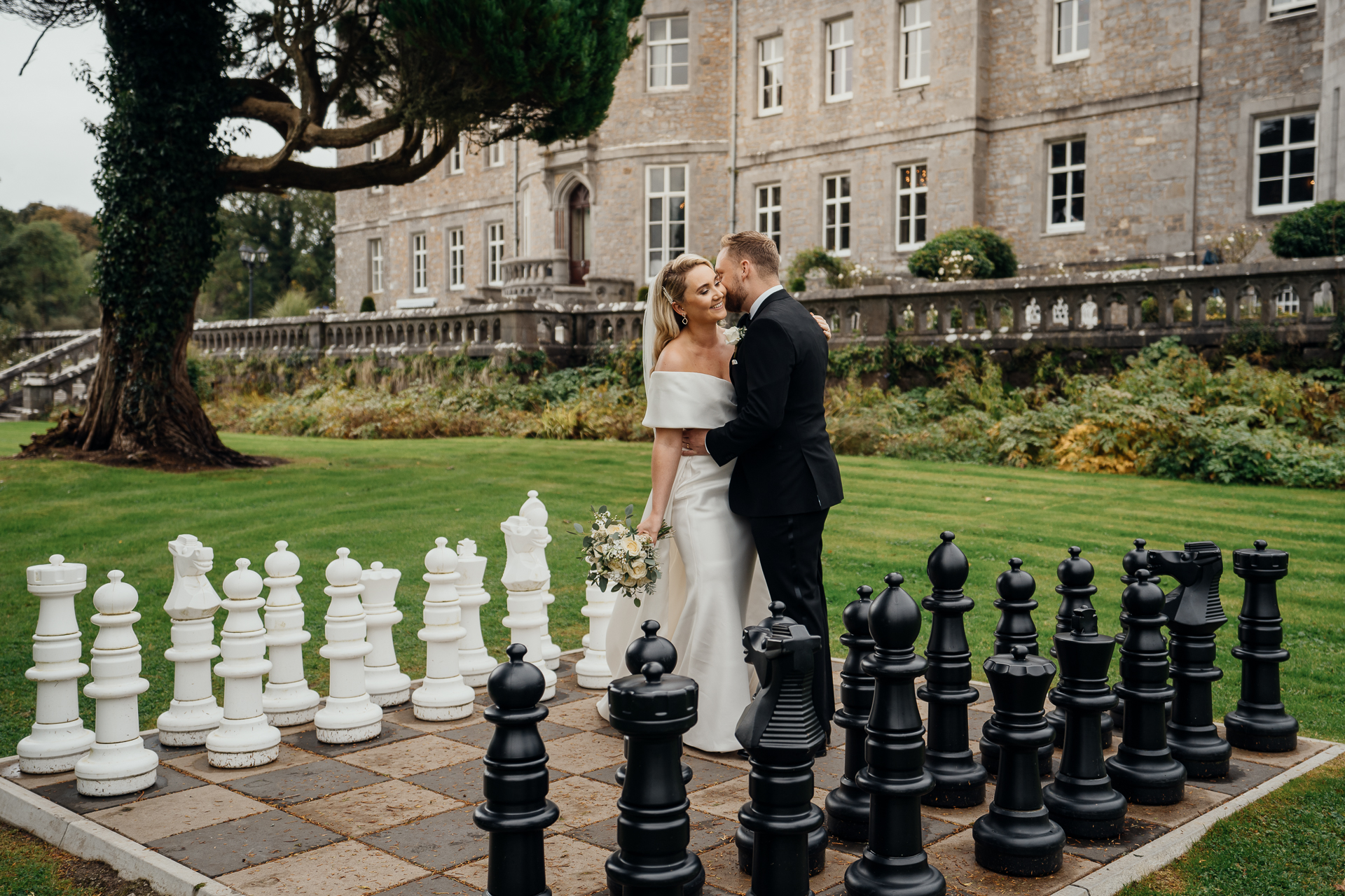 A man and woman in wedding attire kissing in front of a building