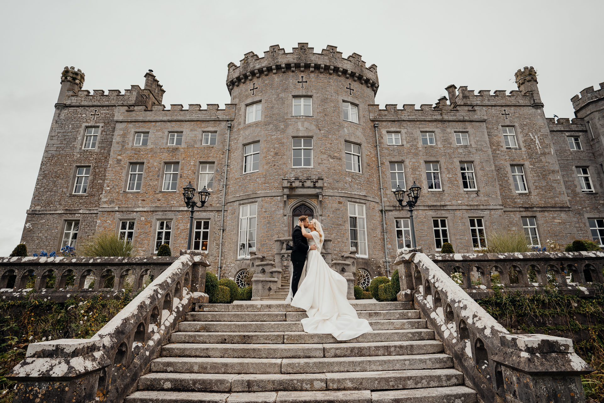 A bride and groom on stairs in front of a large building with Bowes Museum in the background