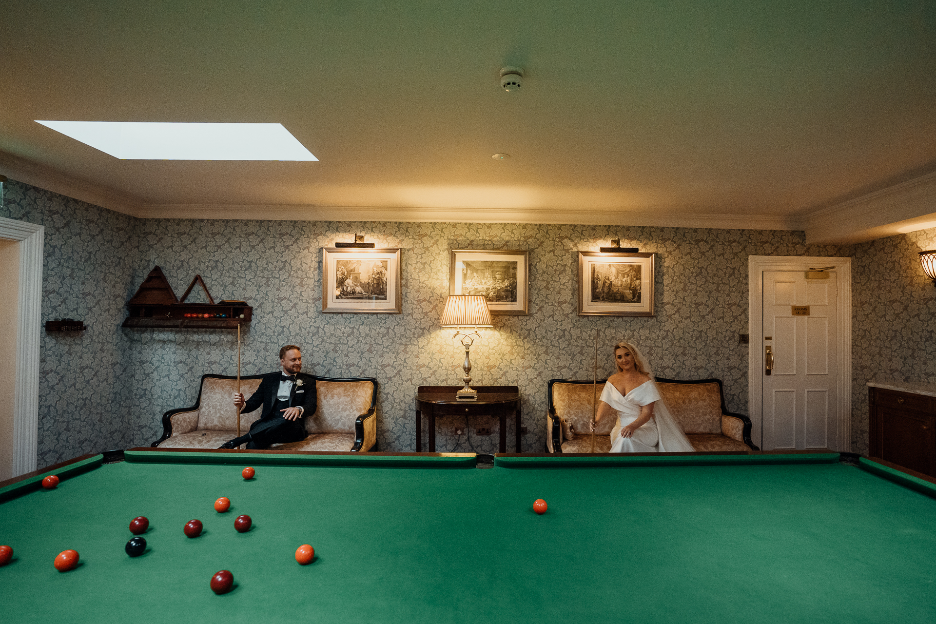 A man and woman sitting on a couch in a room with a pool table and a fireplace