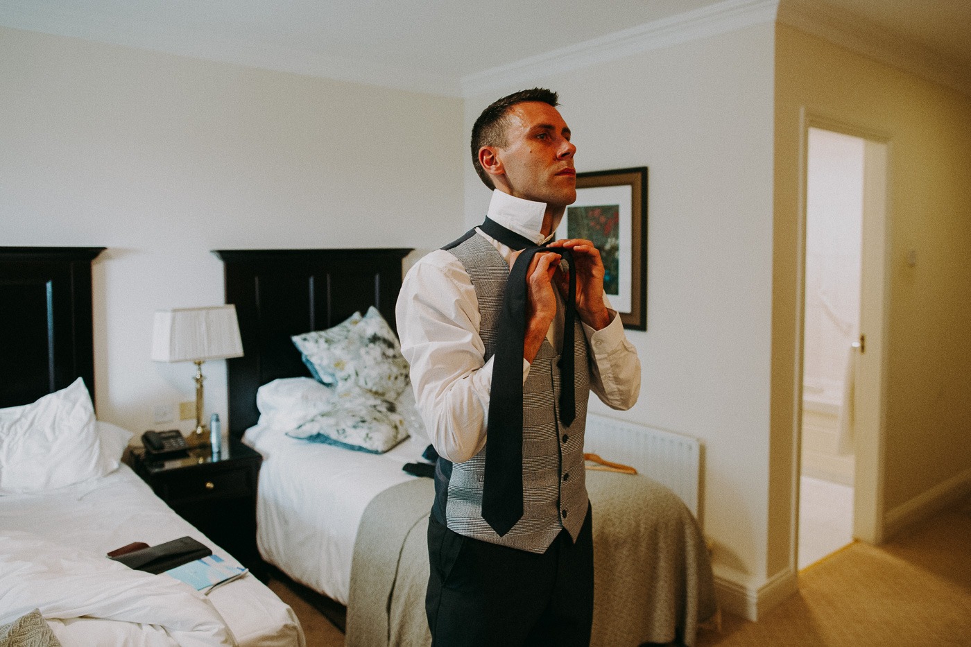 A man wearing a suit and tie standing next to a bed