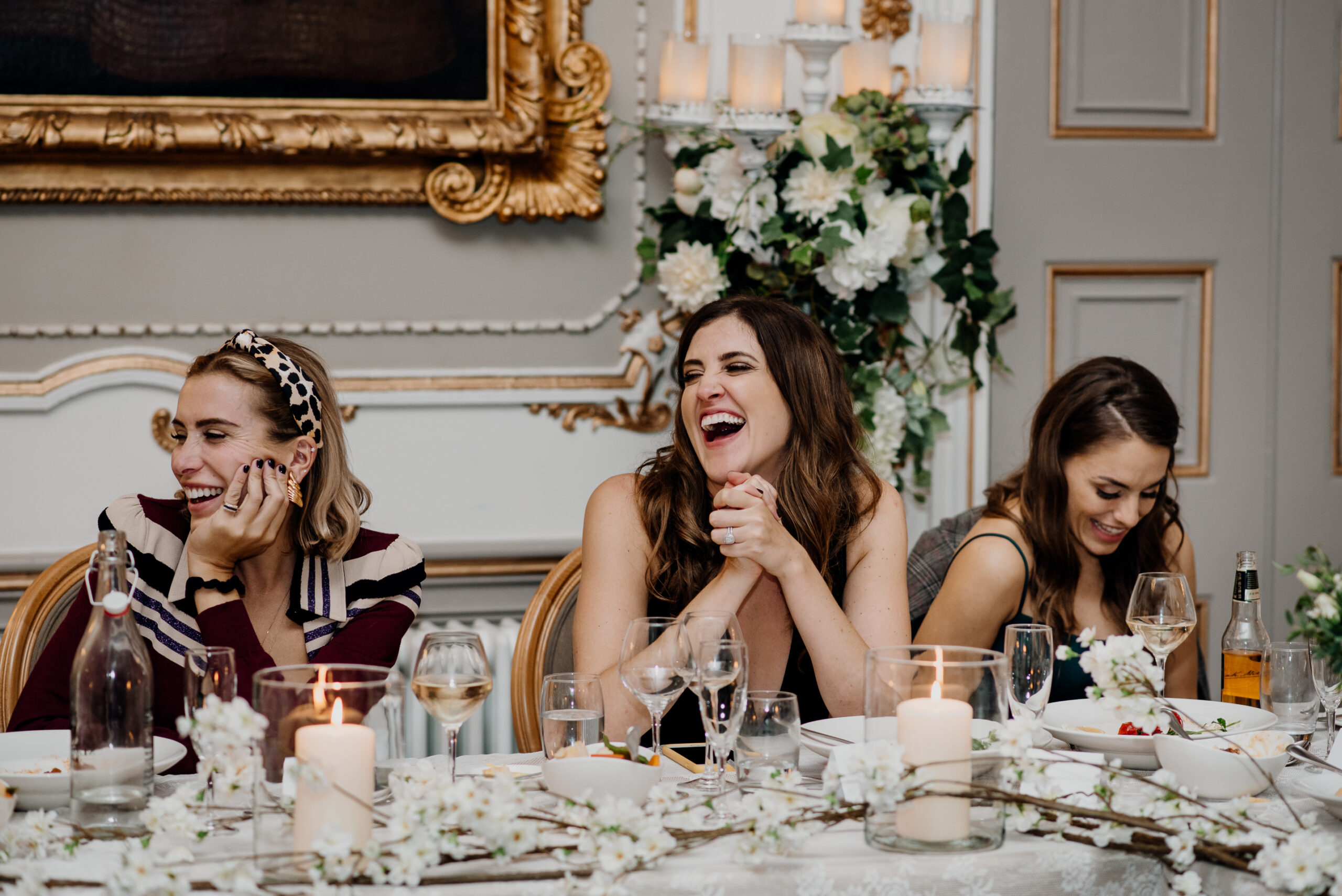 A group of women sitting at a table with wine glasses and flowers