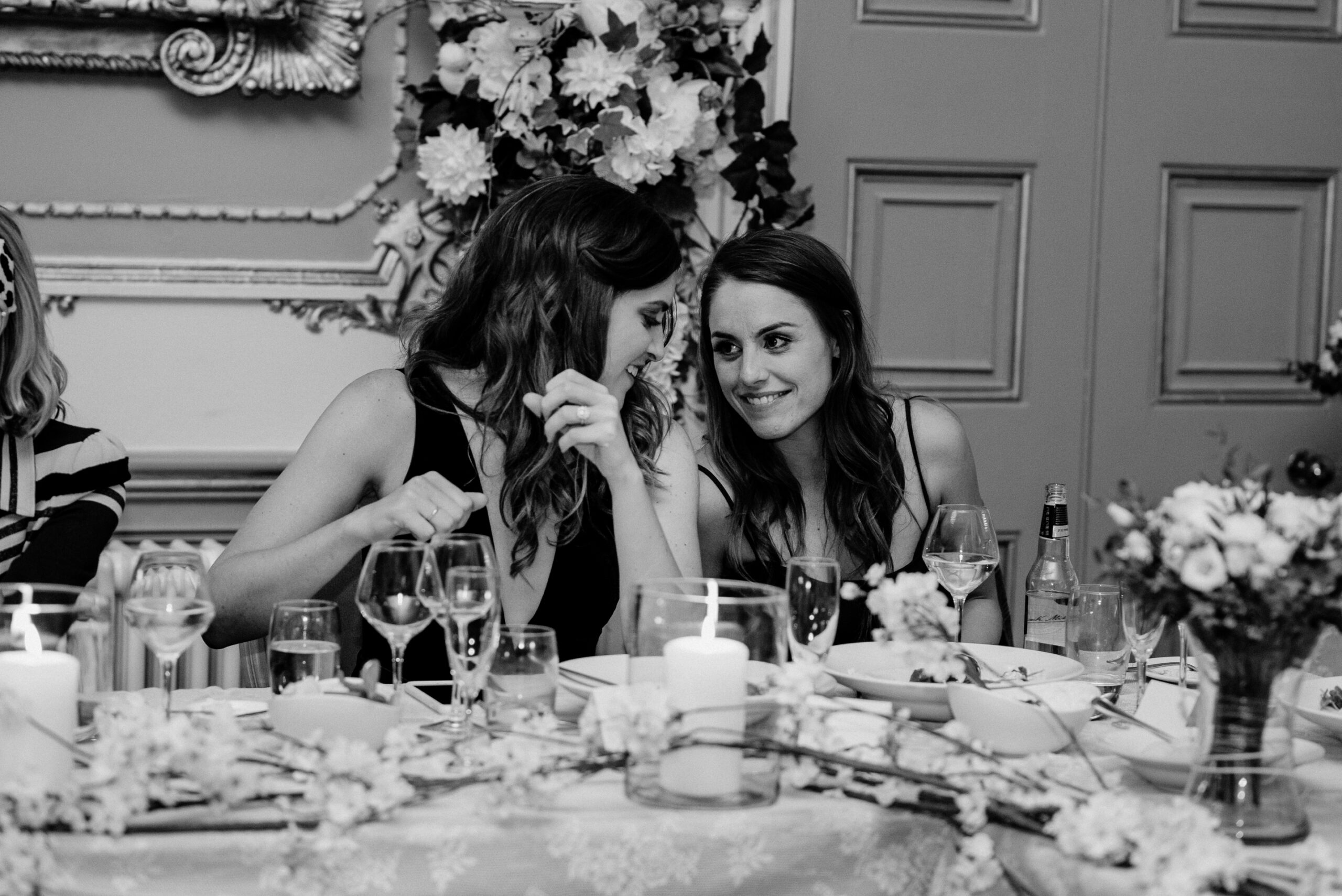 A couple of women sitting at a table with food and drinks