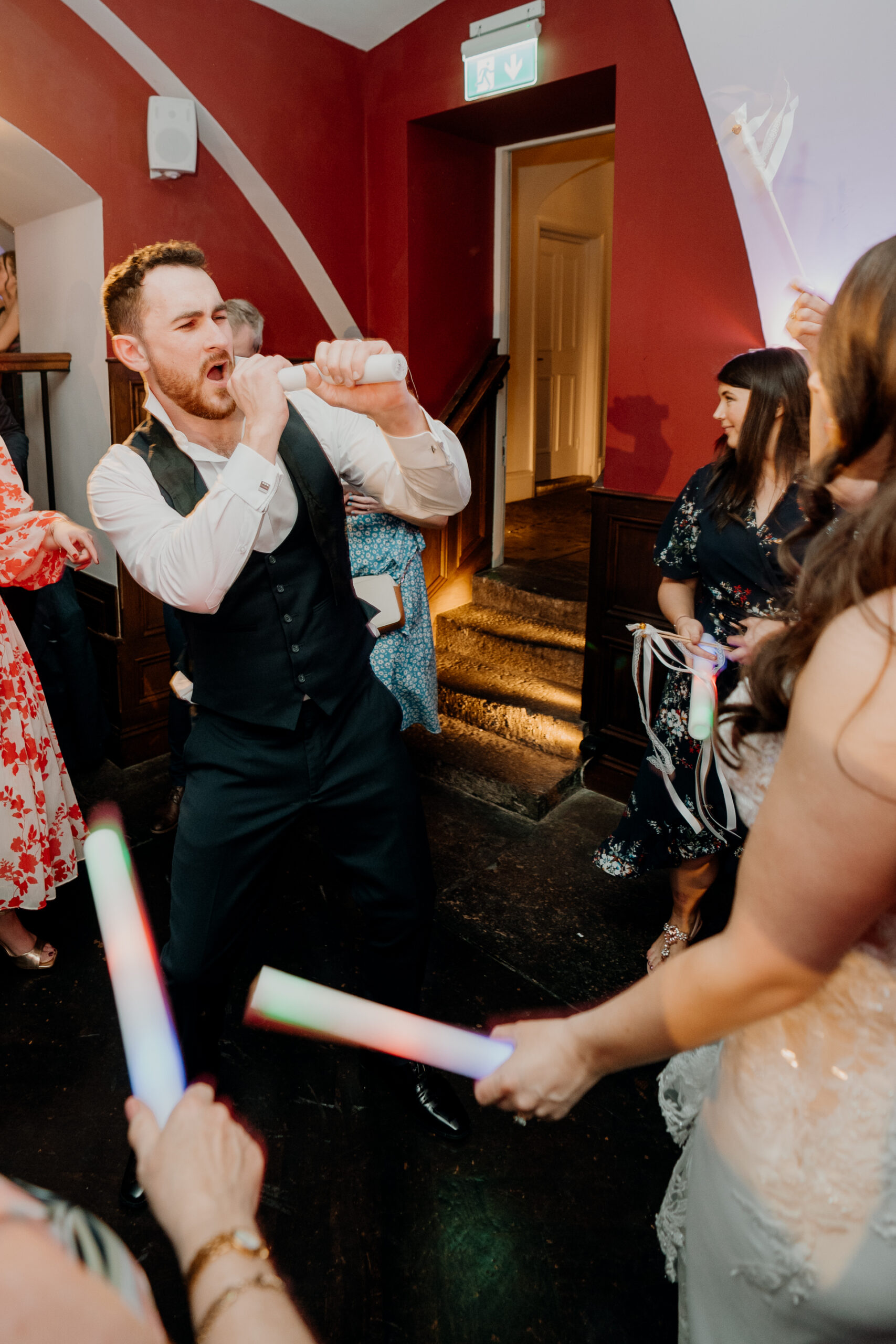 A person in a tuxedo holding a white object in a room with other people