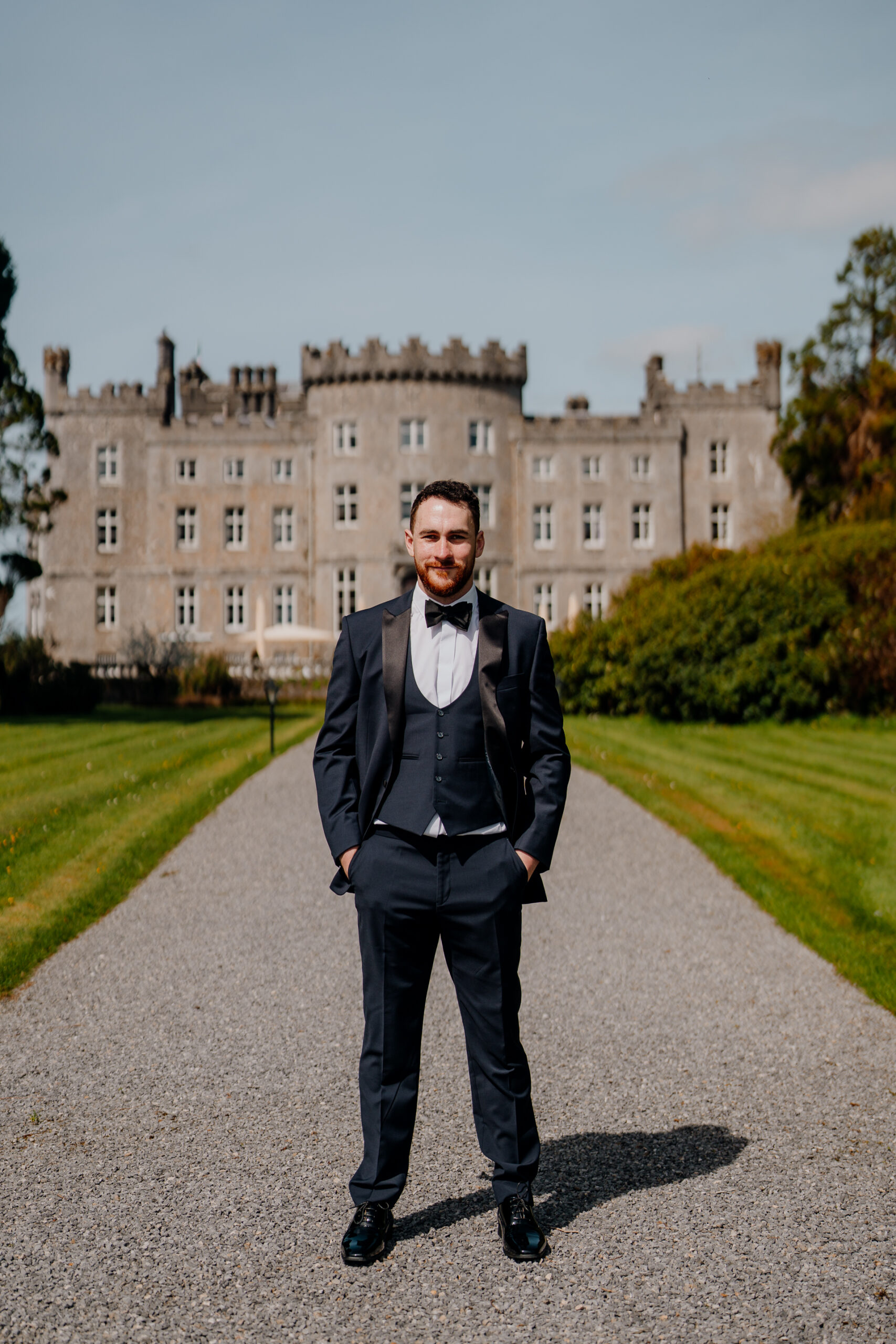 A person in a suit standing on a road in front of a large building