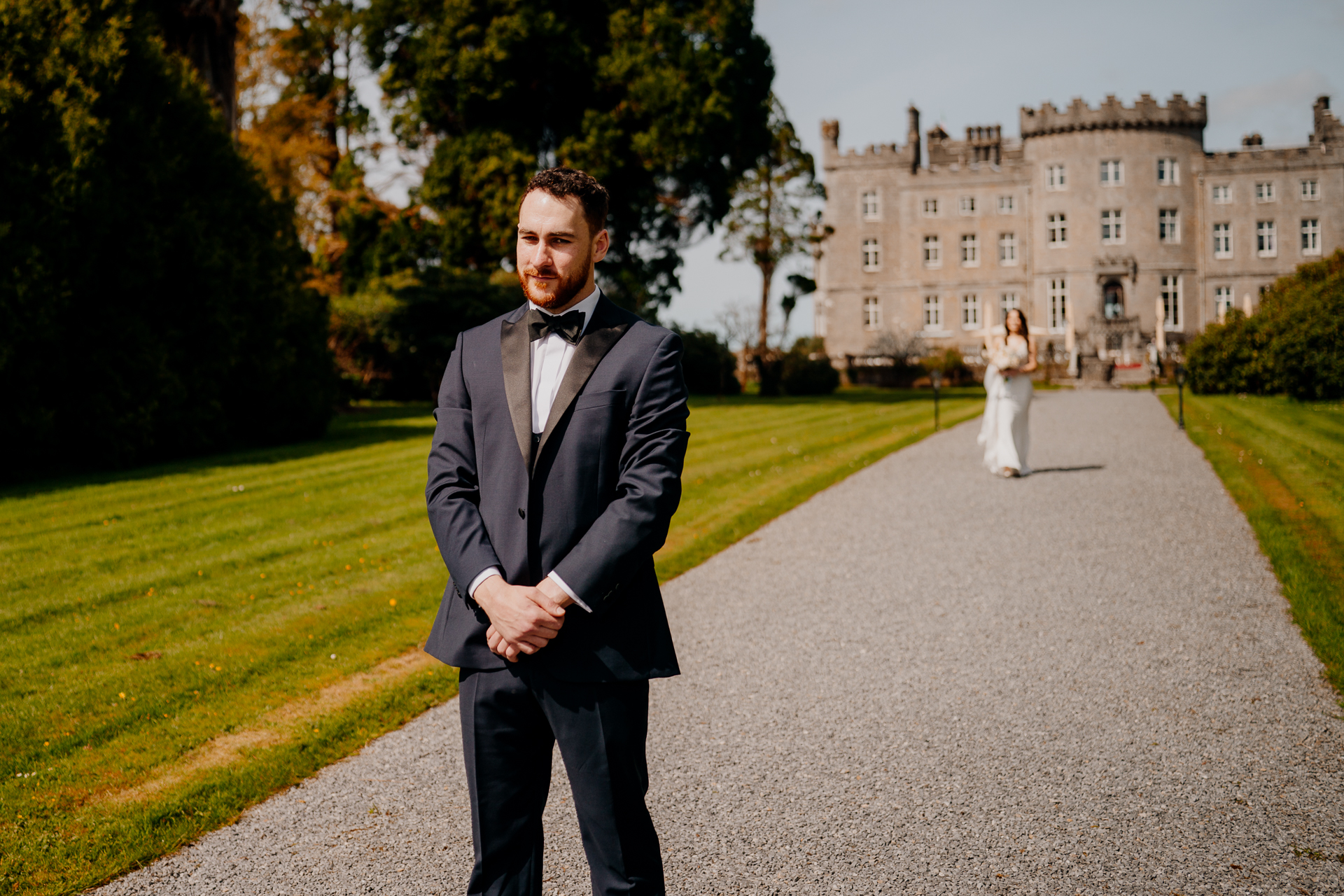 A man in a tuxedo walking down a path with a woman in a dress and a