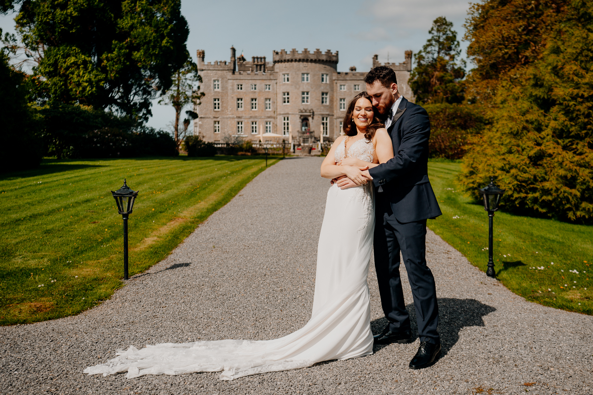 A man and woman in wedding attire kissing on a path in front of a large building