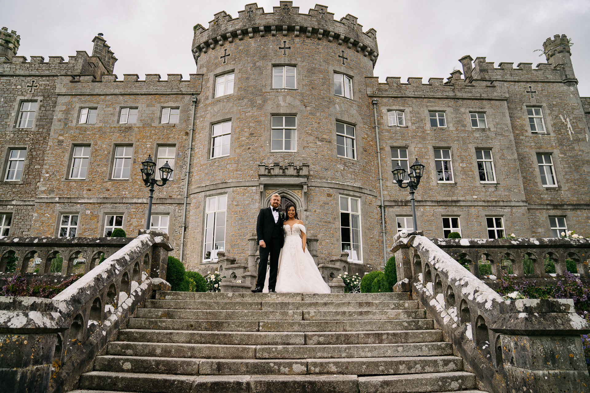 A man and woman in wedding attire standing on stairs in front of a large building