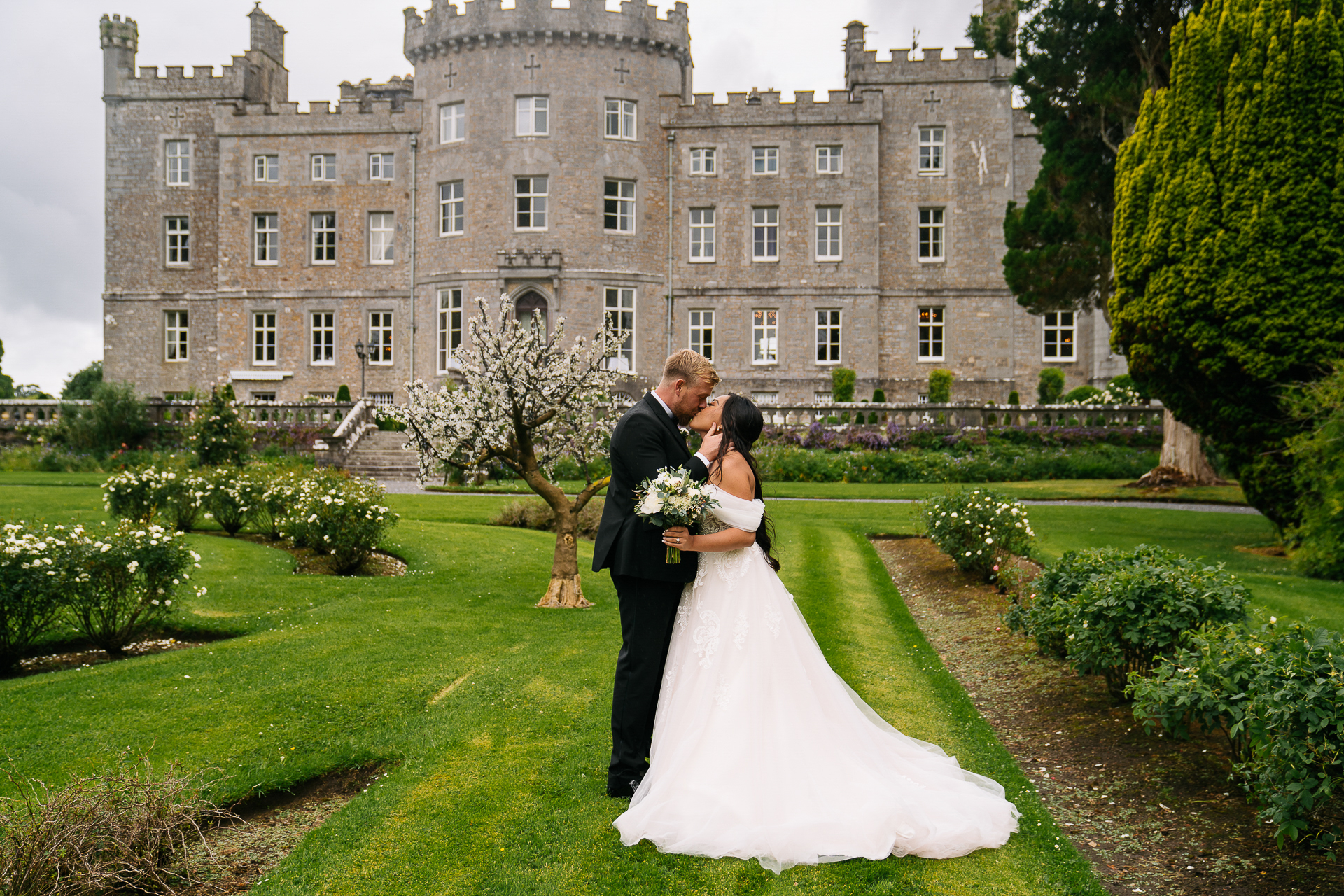 A man and woman in wedding attire kissing in front of a large building