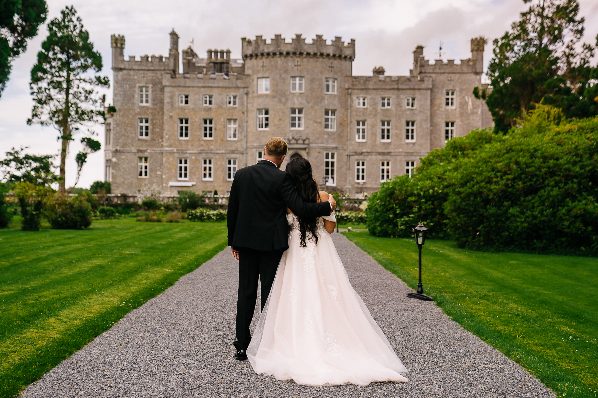 A man and woman in wedding attire walking down a path in front of a large building