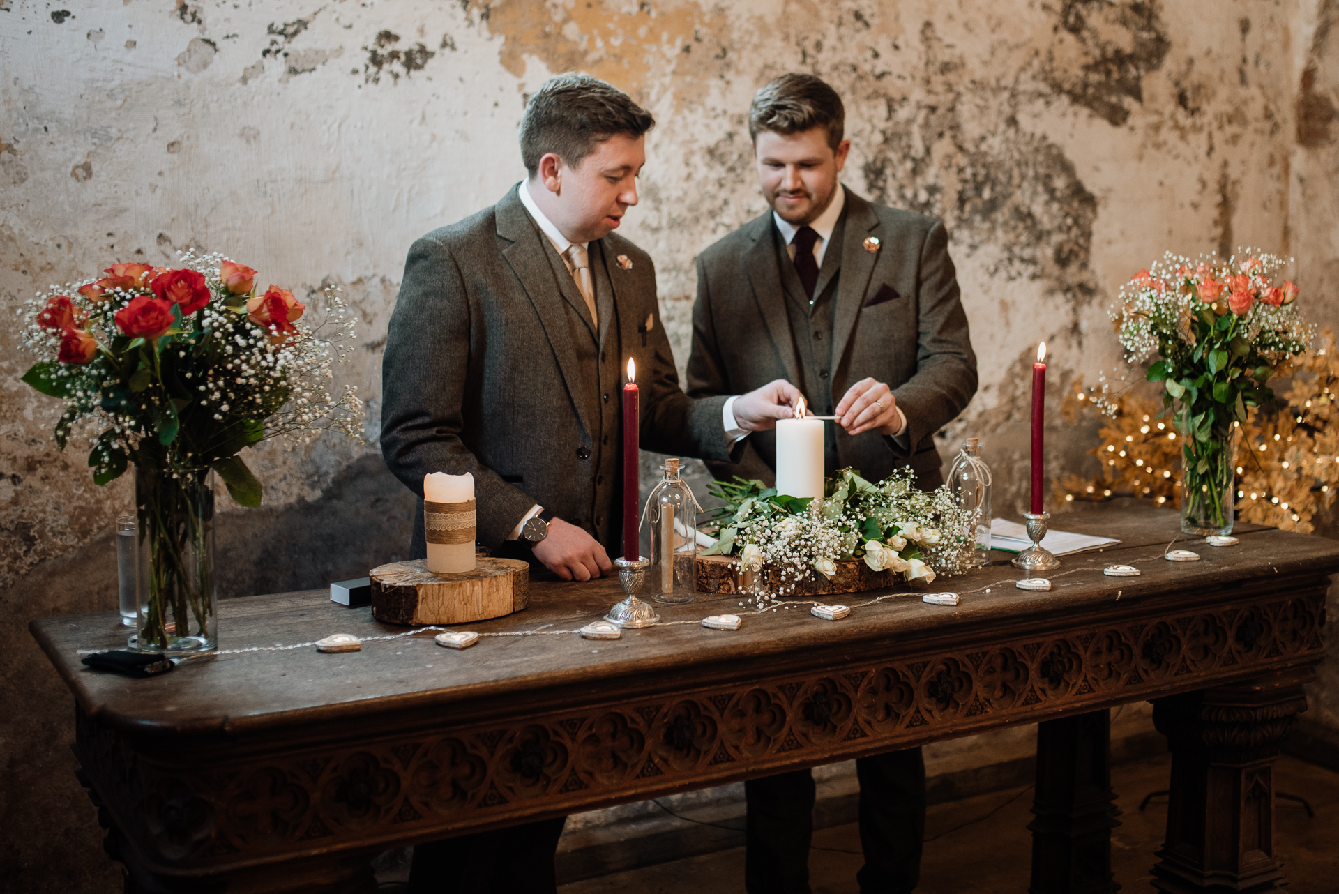 A couple of men sitting at a table with flowers and candles