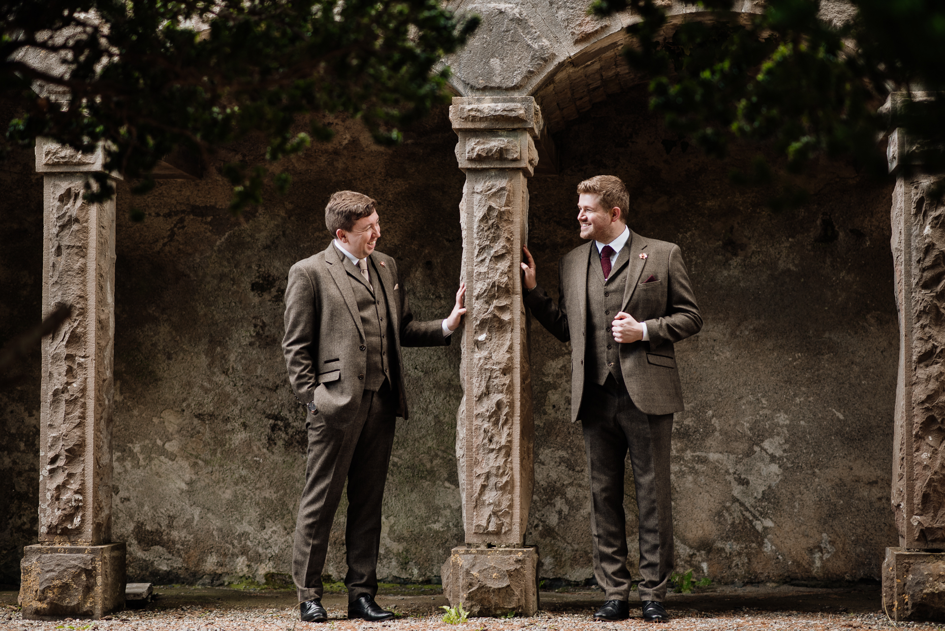 Two men in suits standing next to a stone pillar