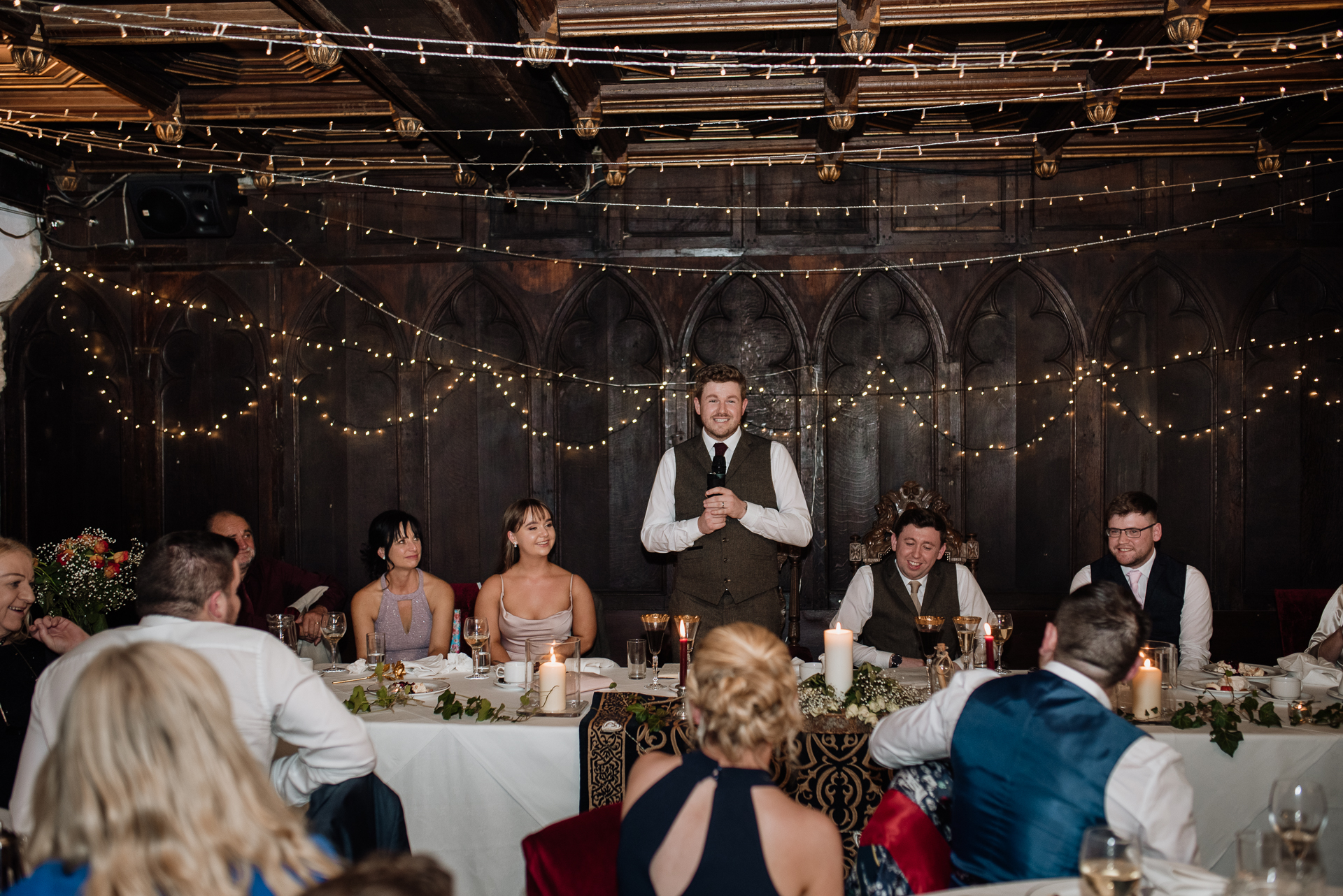 A person in a suit and tie standing in front of a group of people at a dinner table