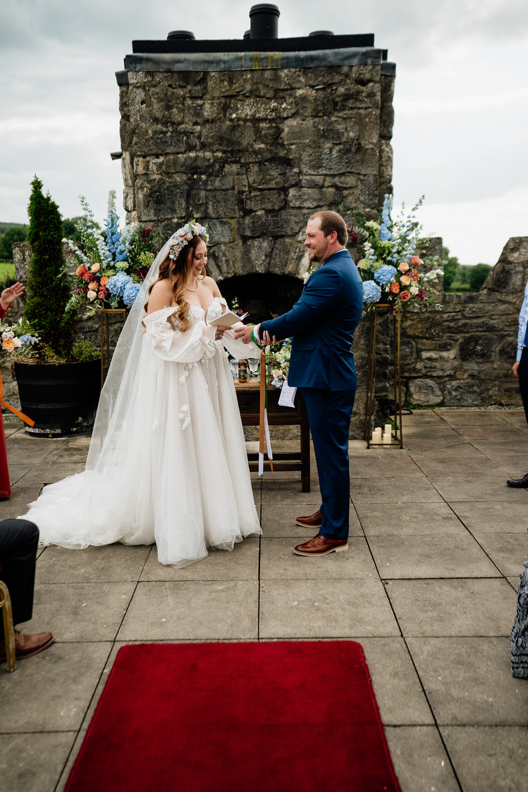 A bride and groom walking down a red carpet in front of a stone building