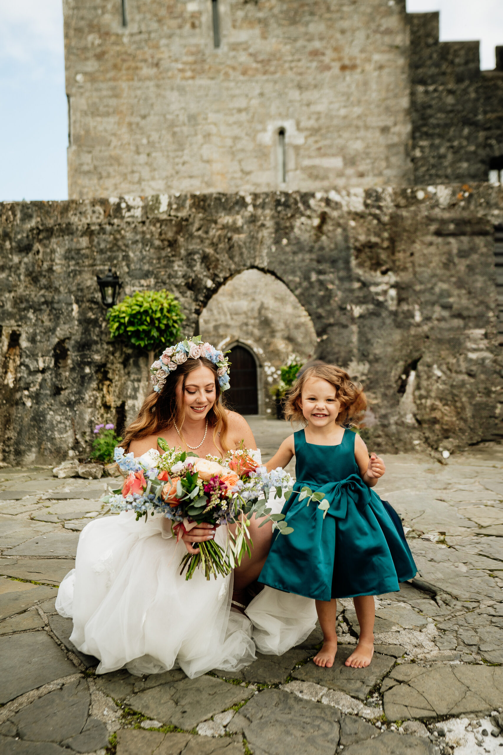 Two girls in dresses sitting on a stone ledge with flowers