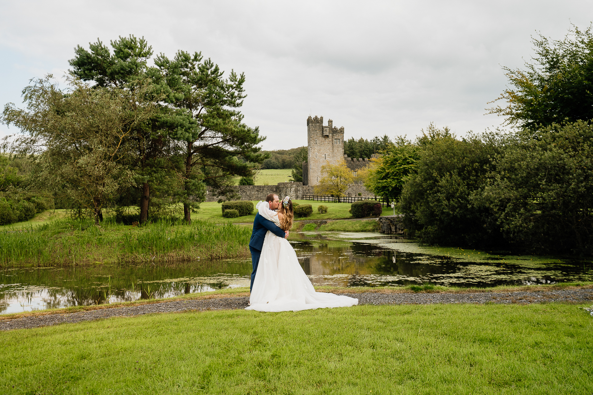 A man and woman kissing in a park with a castle in the background