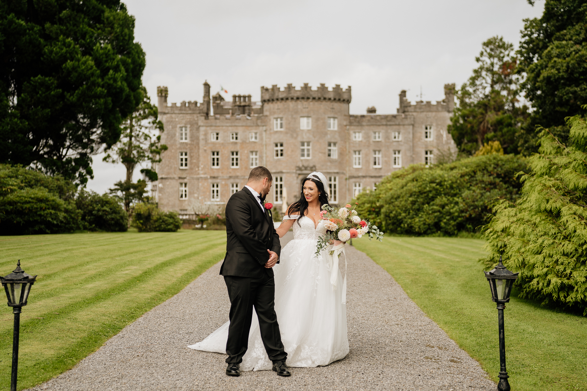 A man and woman in wedding attire walking down a path in front of a large building