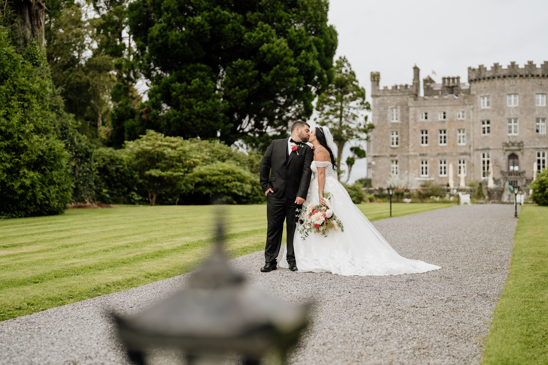 A man and woman in wedding attire kissing on a path with a building in the background