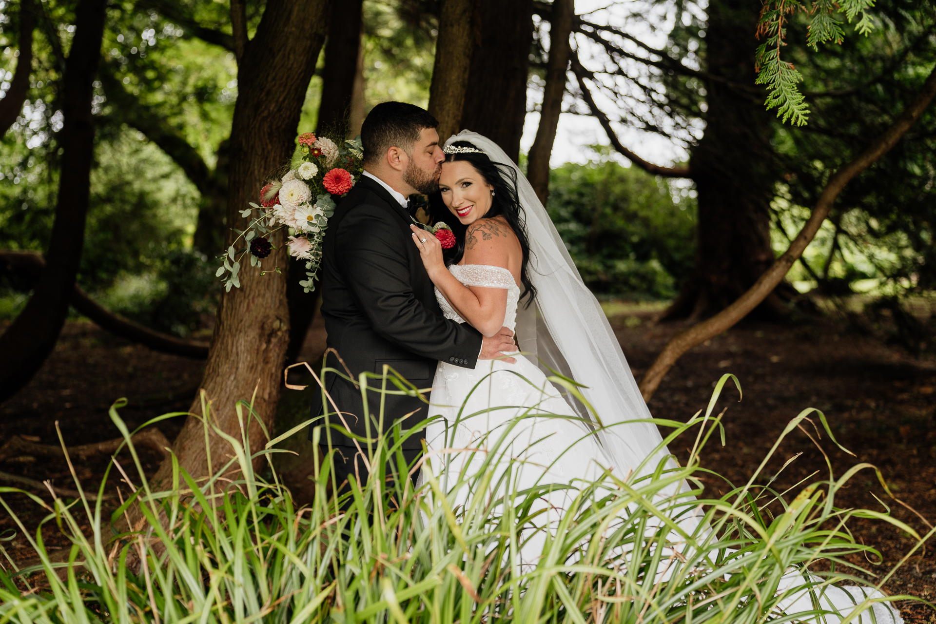 A man and woman in wedding attire kissing in a forest