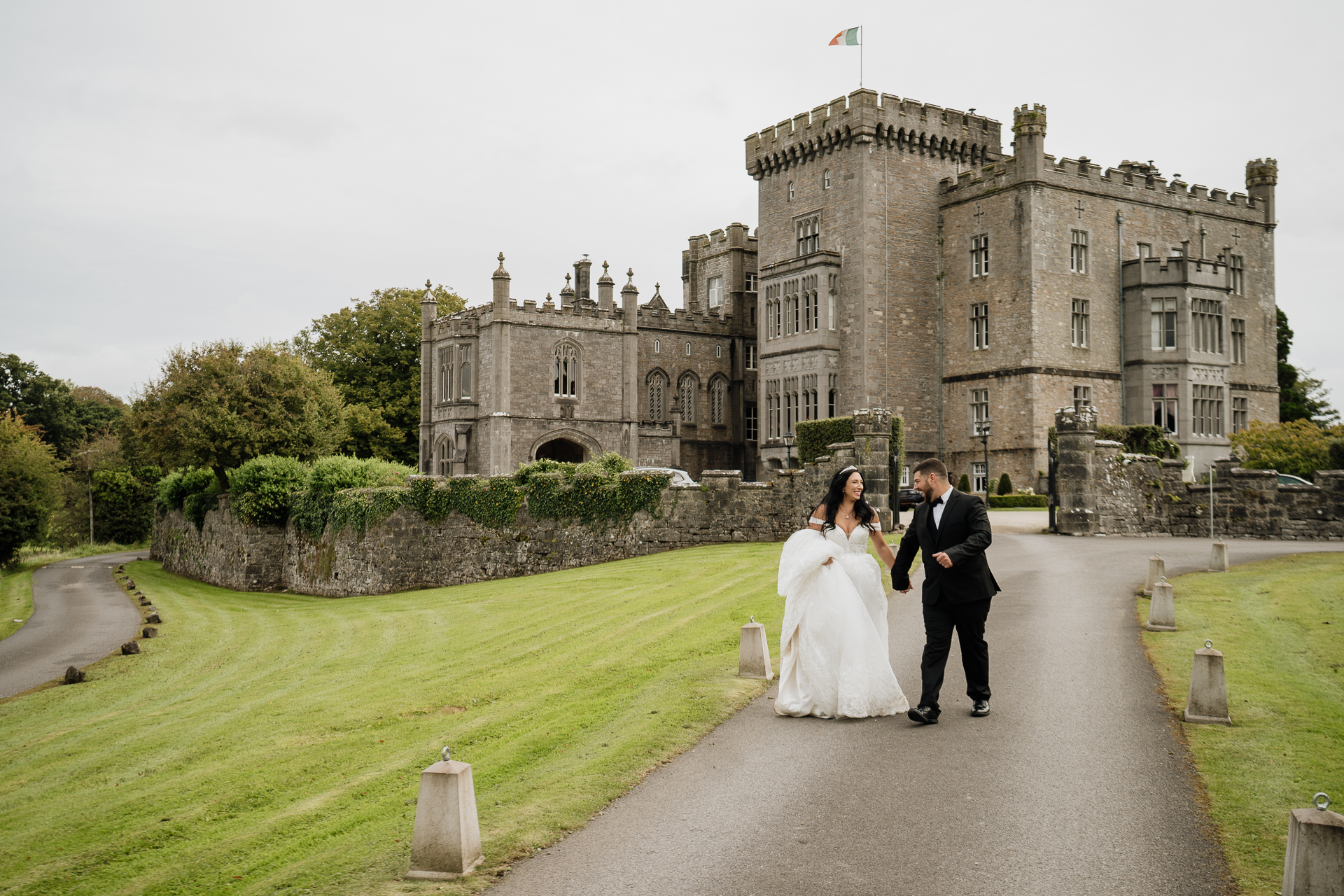 A bride and groom walking down a path in front of a castle