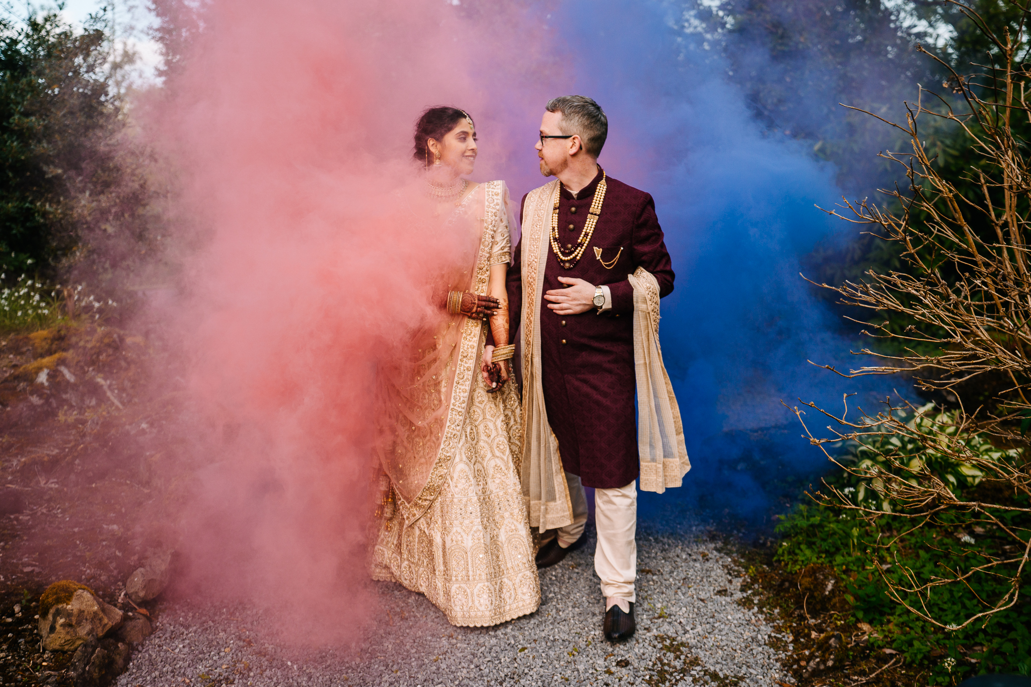 A man and woman in wedding attire kissing in front of a pink and purple background