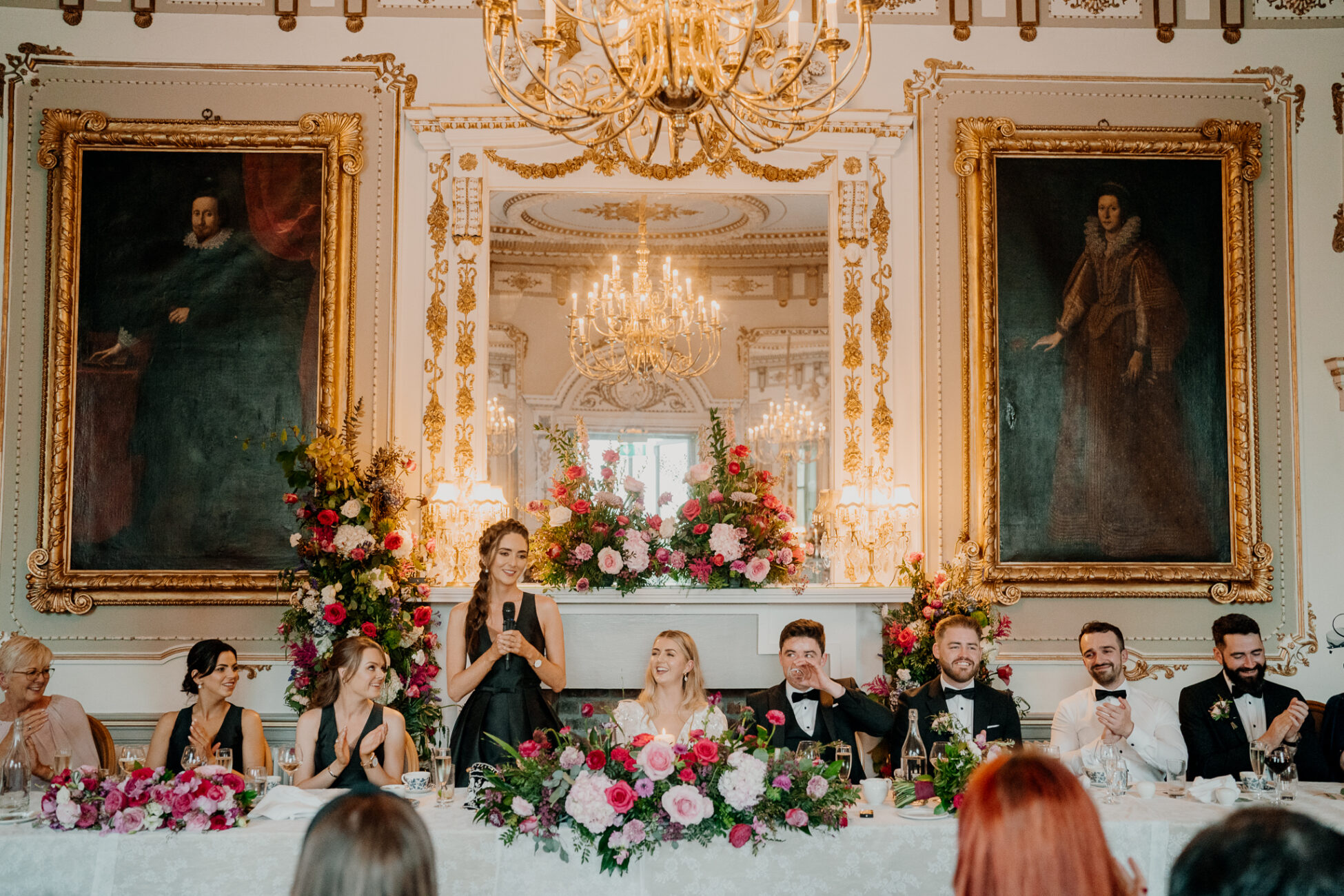 A group of people sitting at a table with flowers in front of a painting