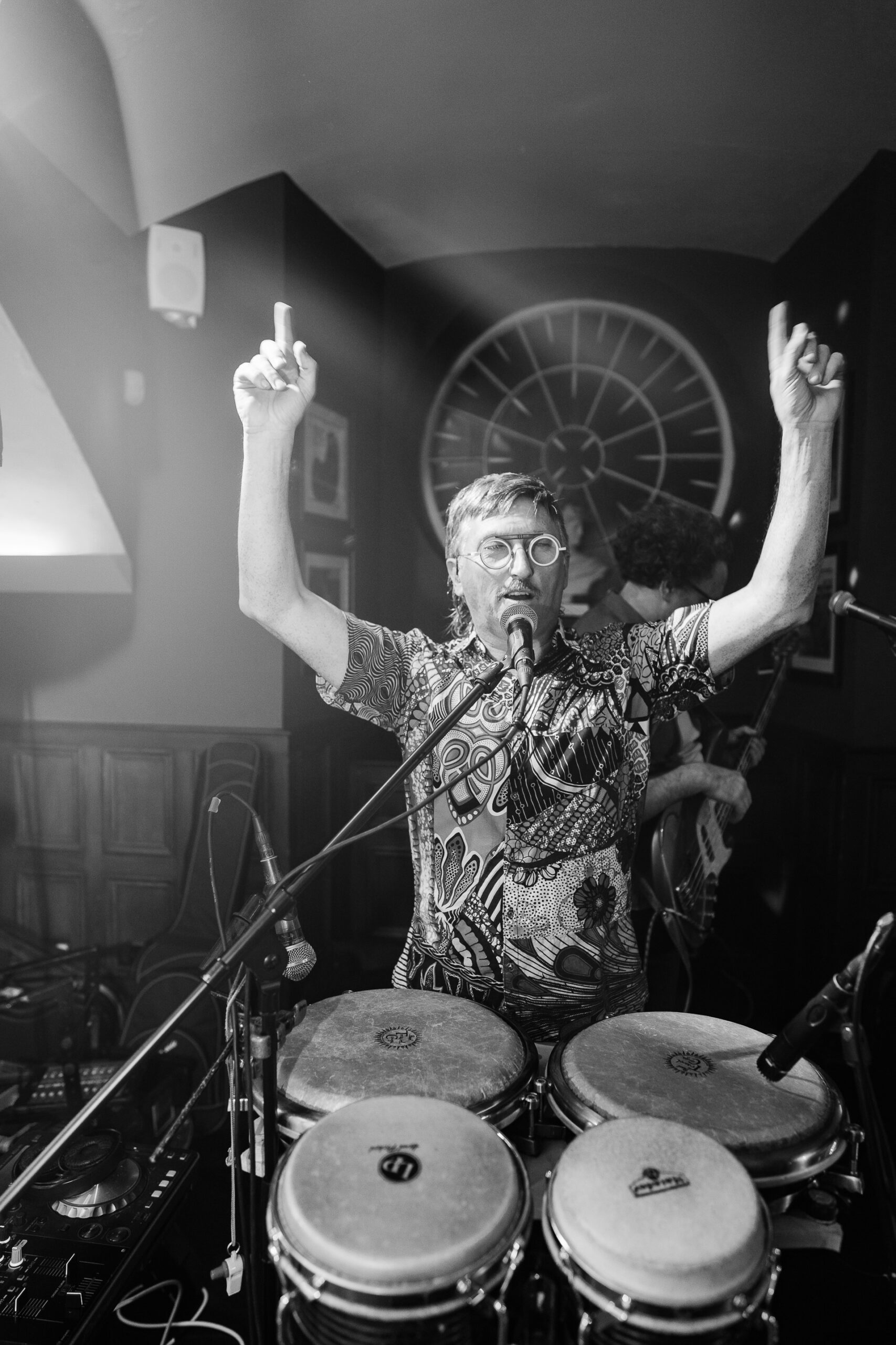 A person with the arms raised and a drum set in front of him