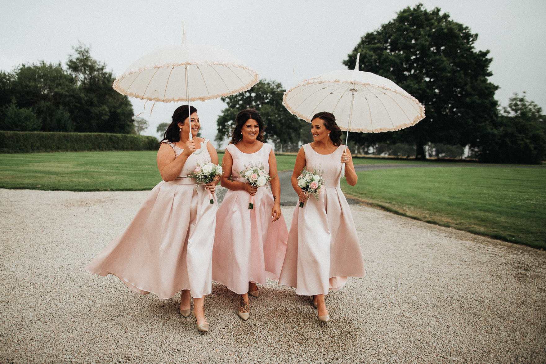 three bridesmaids in pink braidsmaid dresses holding a white umbrellas at irish wedding 