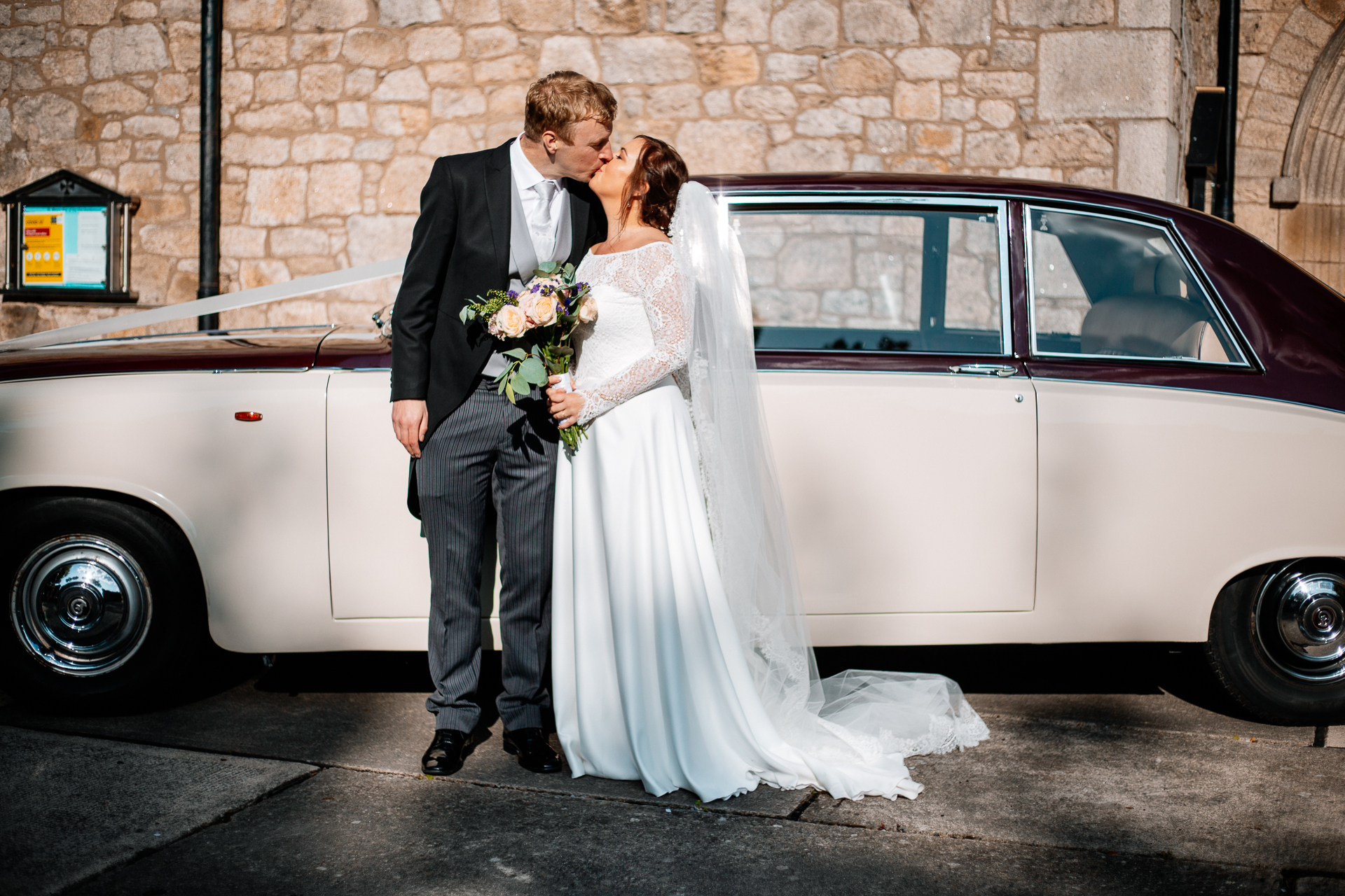 A man and woman kissing in front of a car