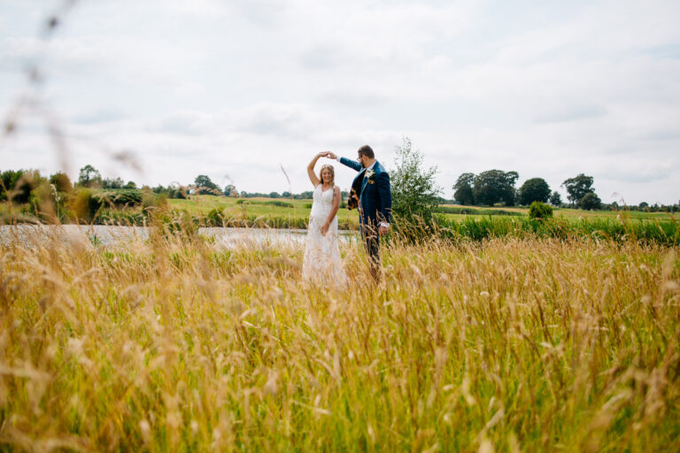 A man and woman standing in a field of tall grass with a cloudy sky