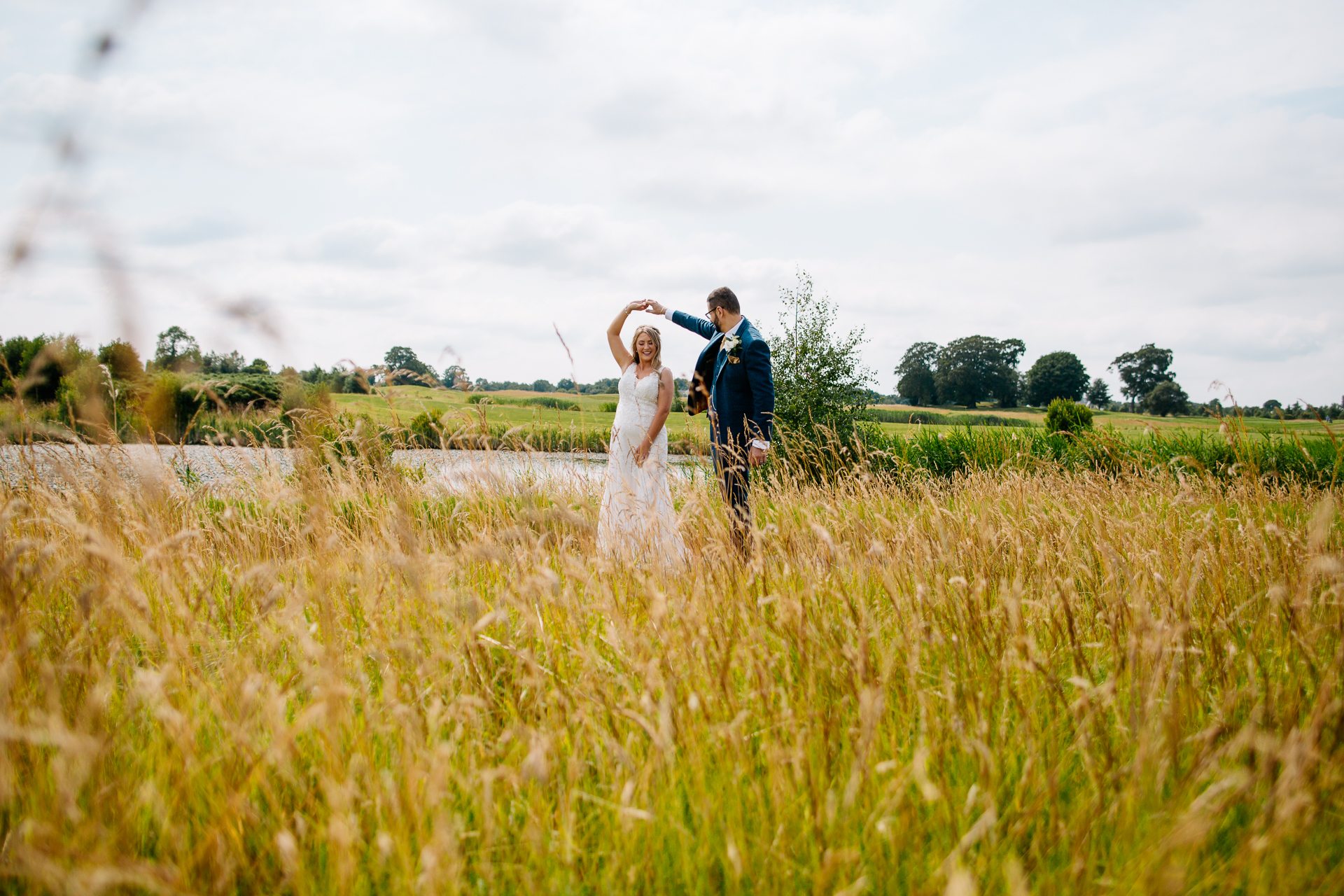 A man and woman standing in a field of tall grass with a cloudy sky