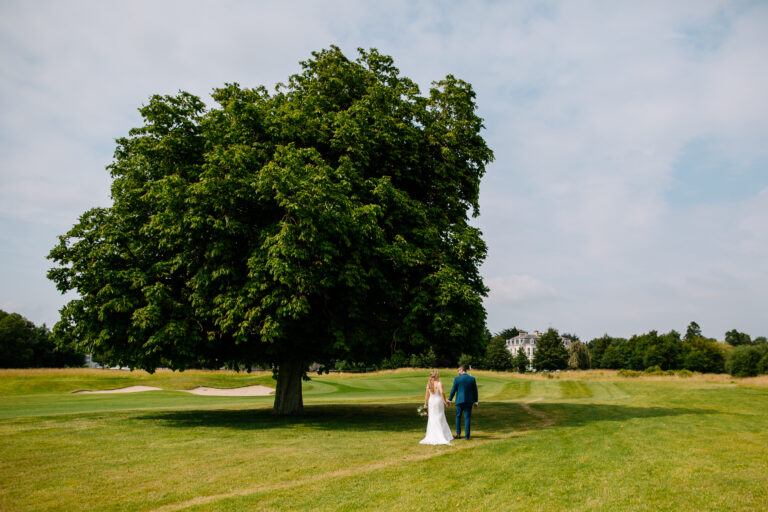 A man and woman walking in a field with a large tree