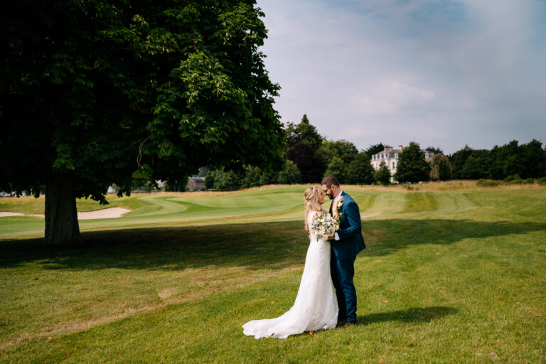 A man and woman kissing in a field with a tree and a house