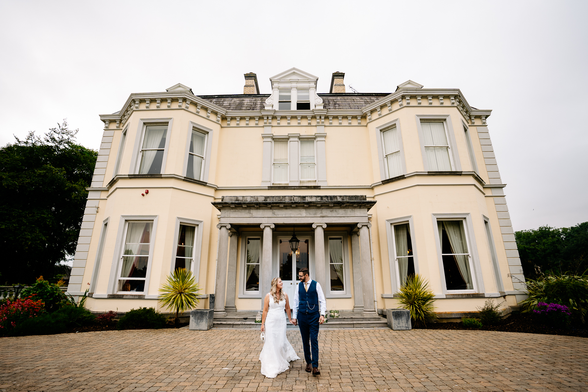 A man and woman posing in front of a large white house