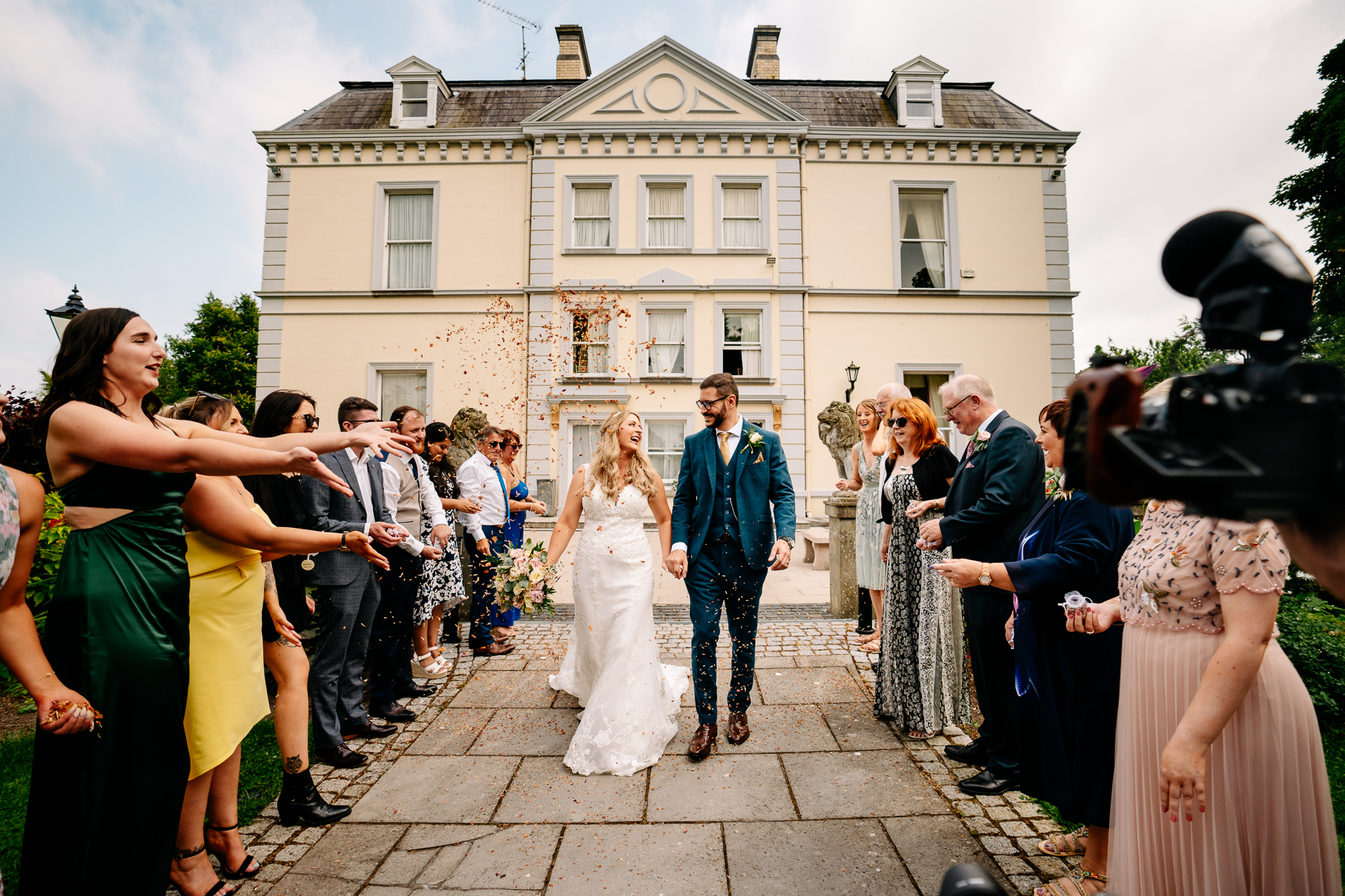 A bride and groom walking down a sidewalk with a crowd watching