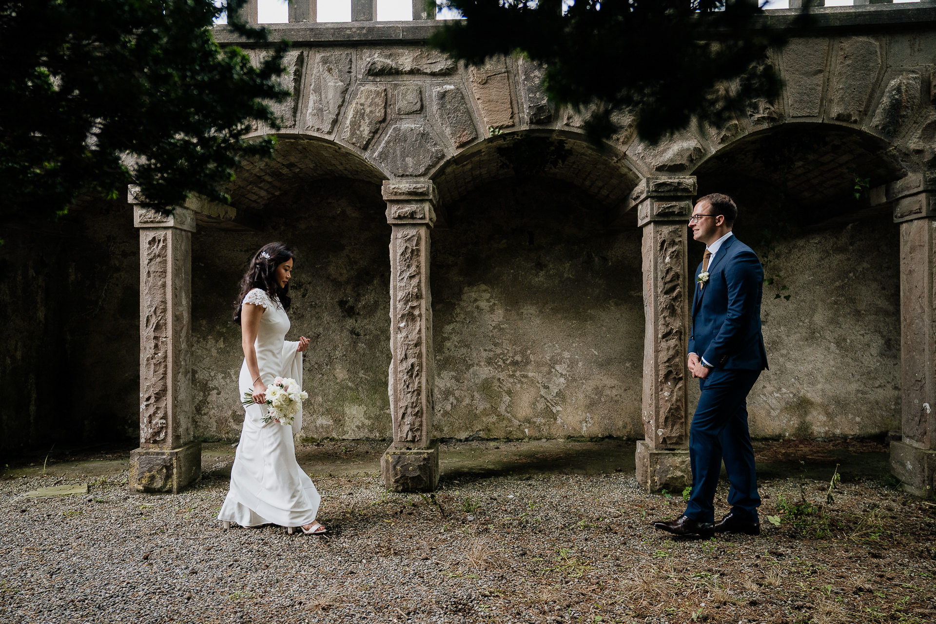 A man and woman walking down a path with a stone arch behind them