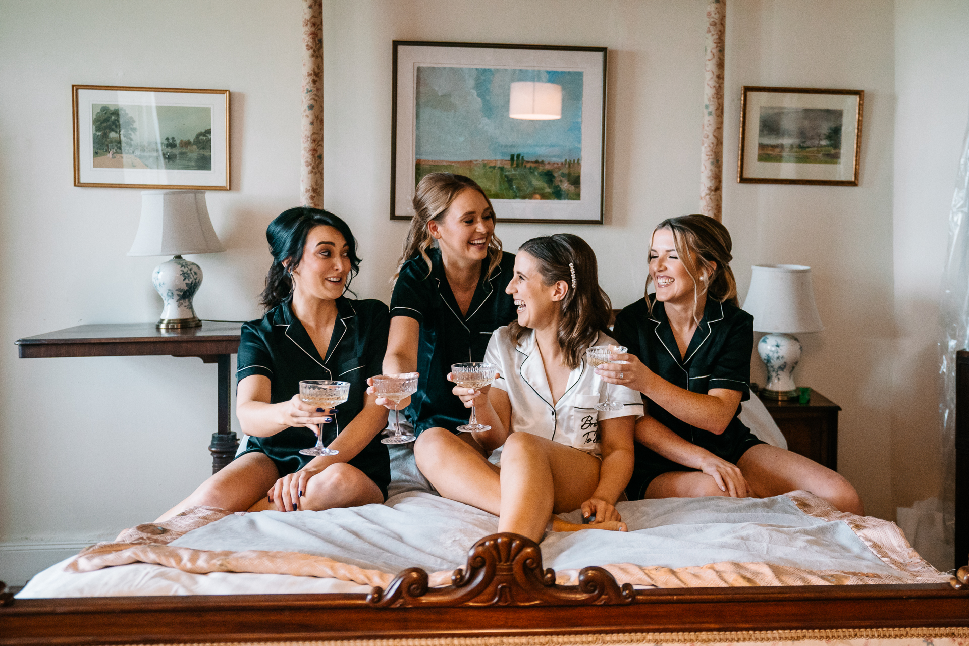 A group of women sitting on a bed holding wine glasses