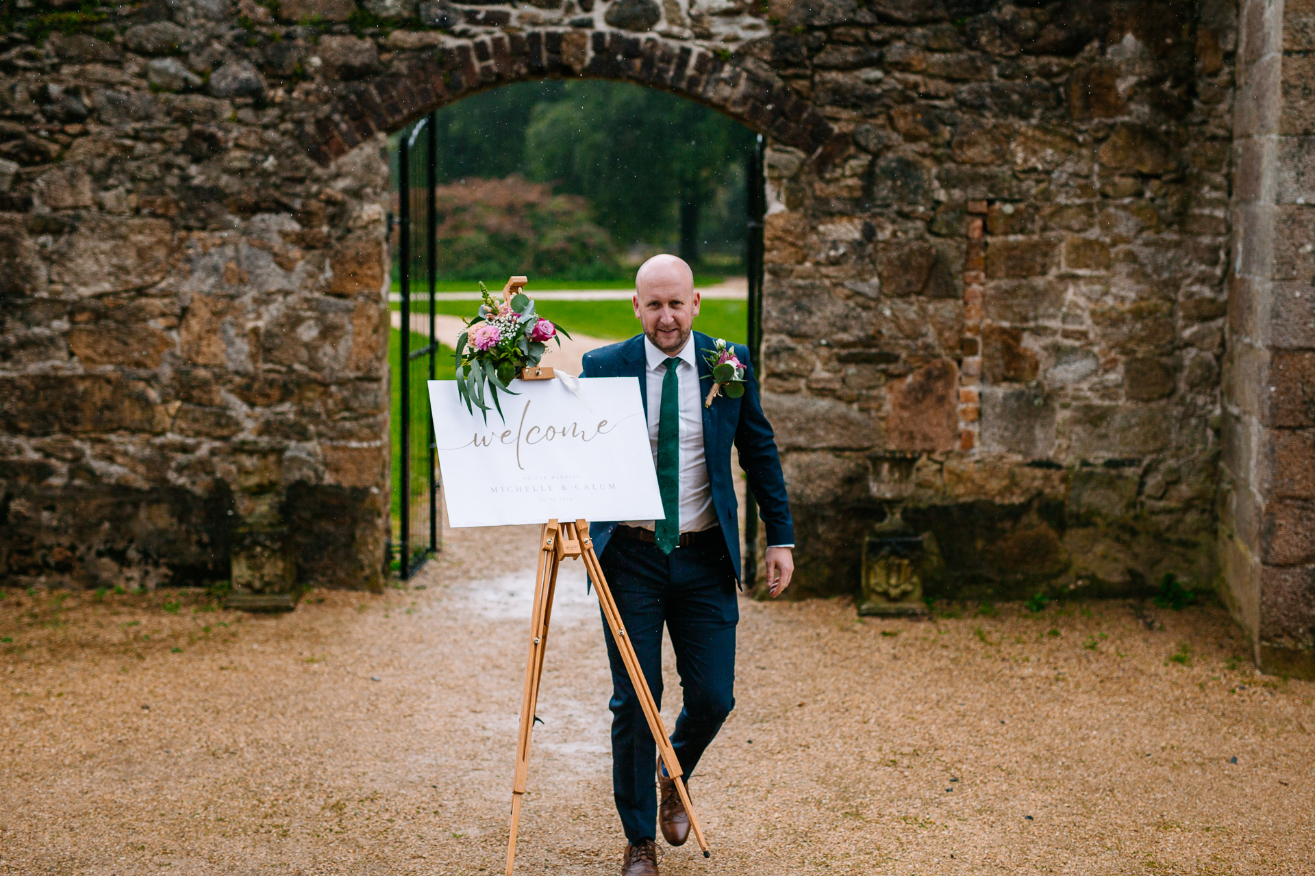 A person in a suit holding a sign in front of a stone archway