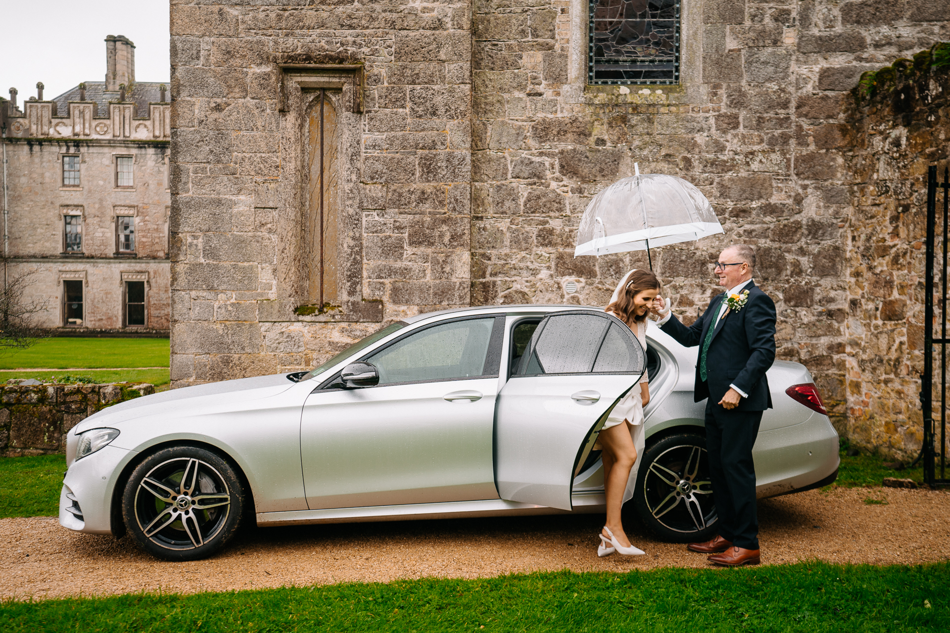 A man and woman standing next to a car with an umbrella