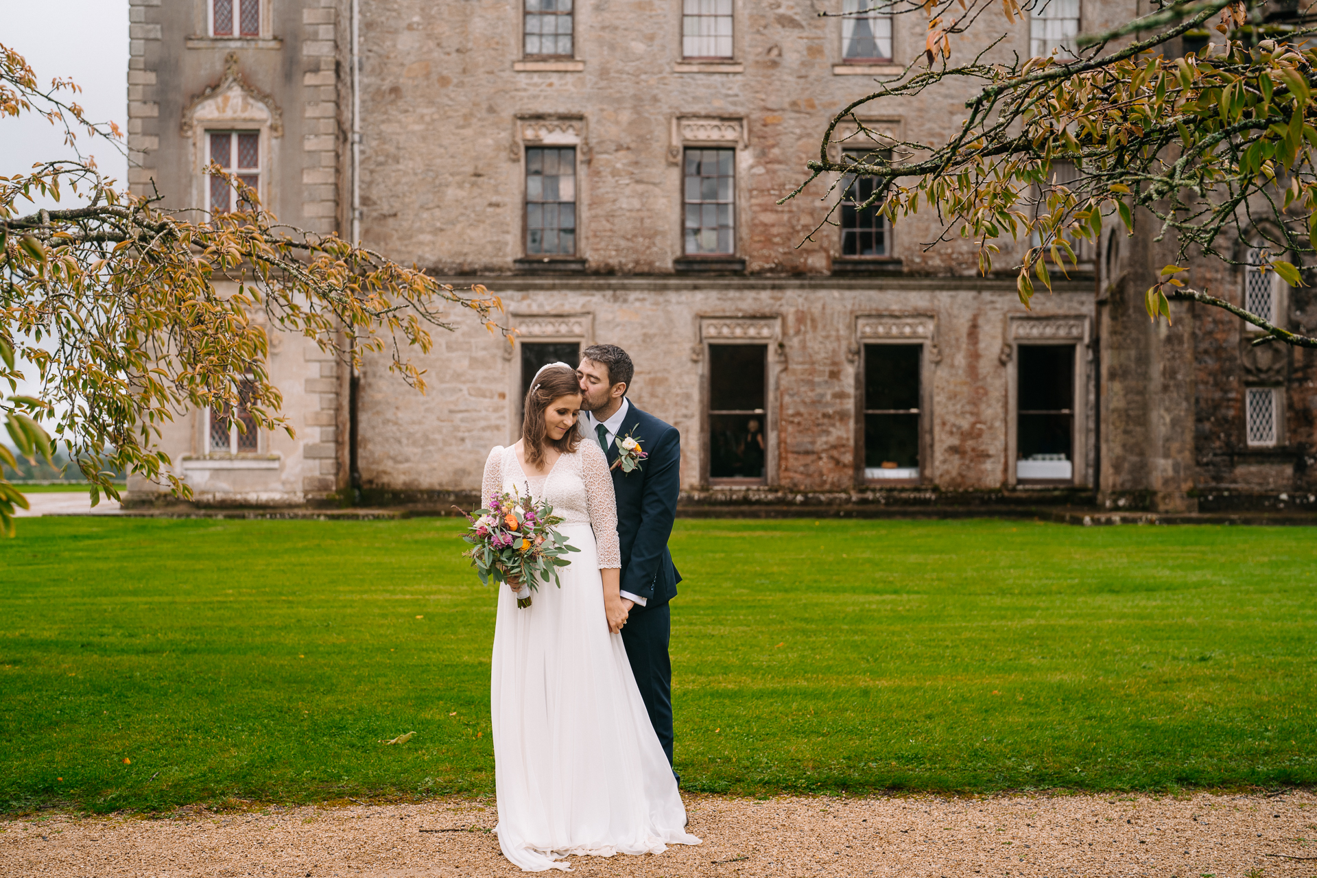 A man and woman in wedding attire kissing in front of a building