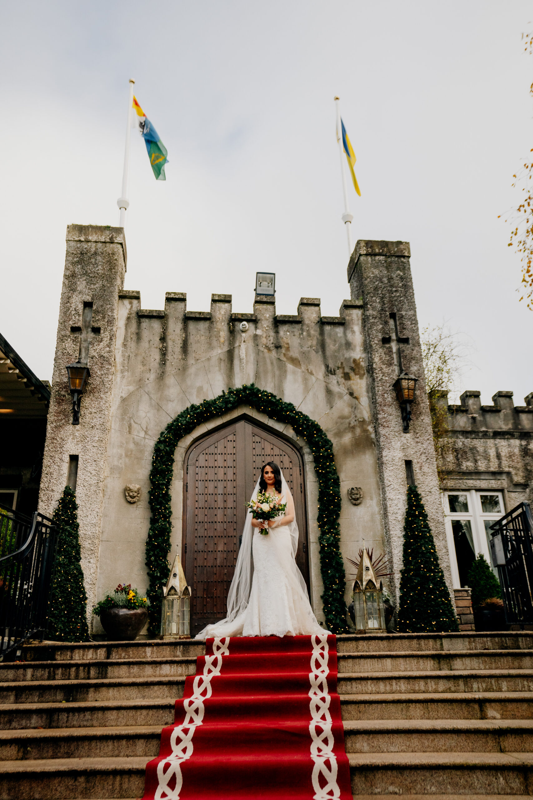 A person in a white dress standing on a staircase in front of a stone building with flags