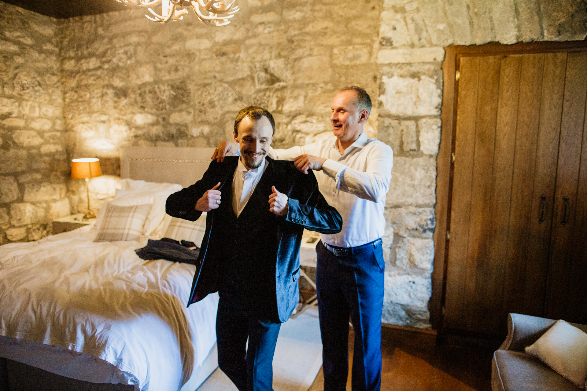 A group of men standing in a room with a bed and a lamp