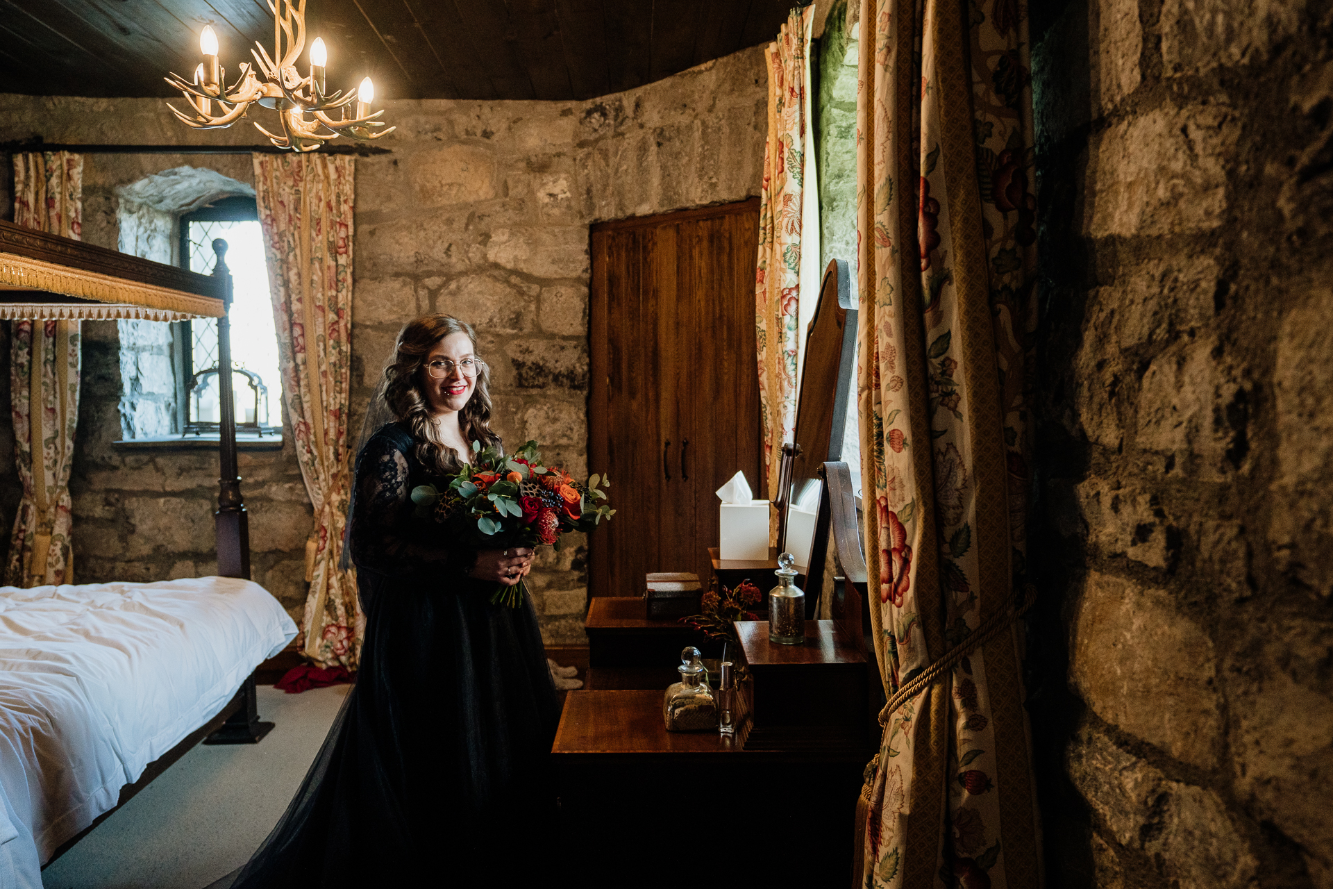 A person in a black dress holding flowers in a room with a mirror