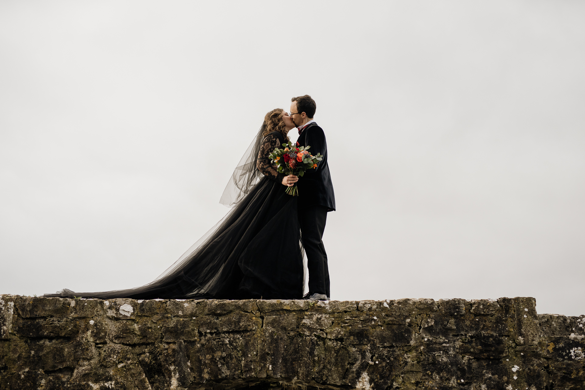 A man and woman kissing on a stone wall