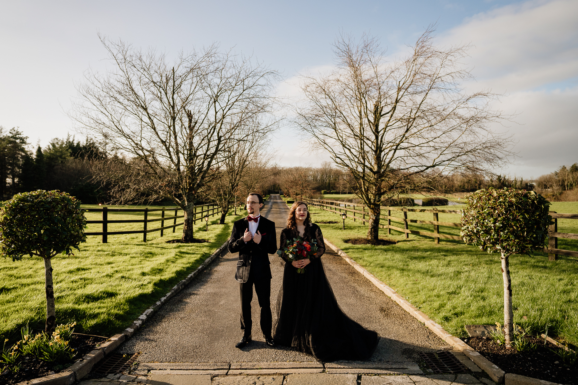 A man and woman posing for a picture on a path with trees and grass