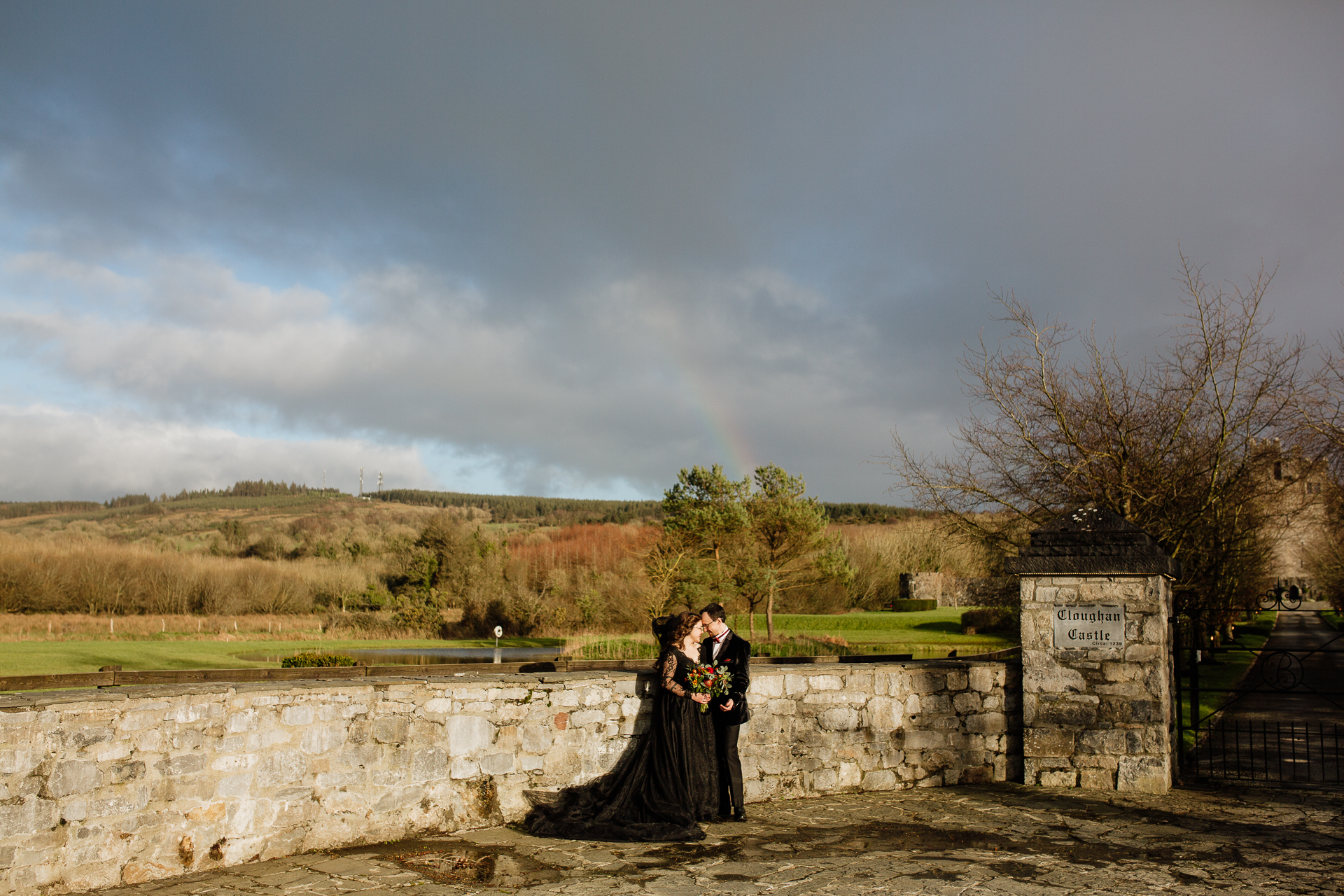 A man and woman standing on a stone wall with a river and trees in the background